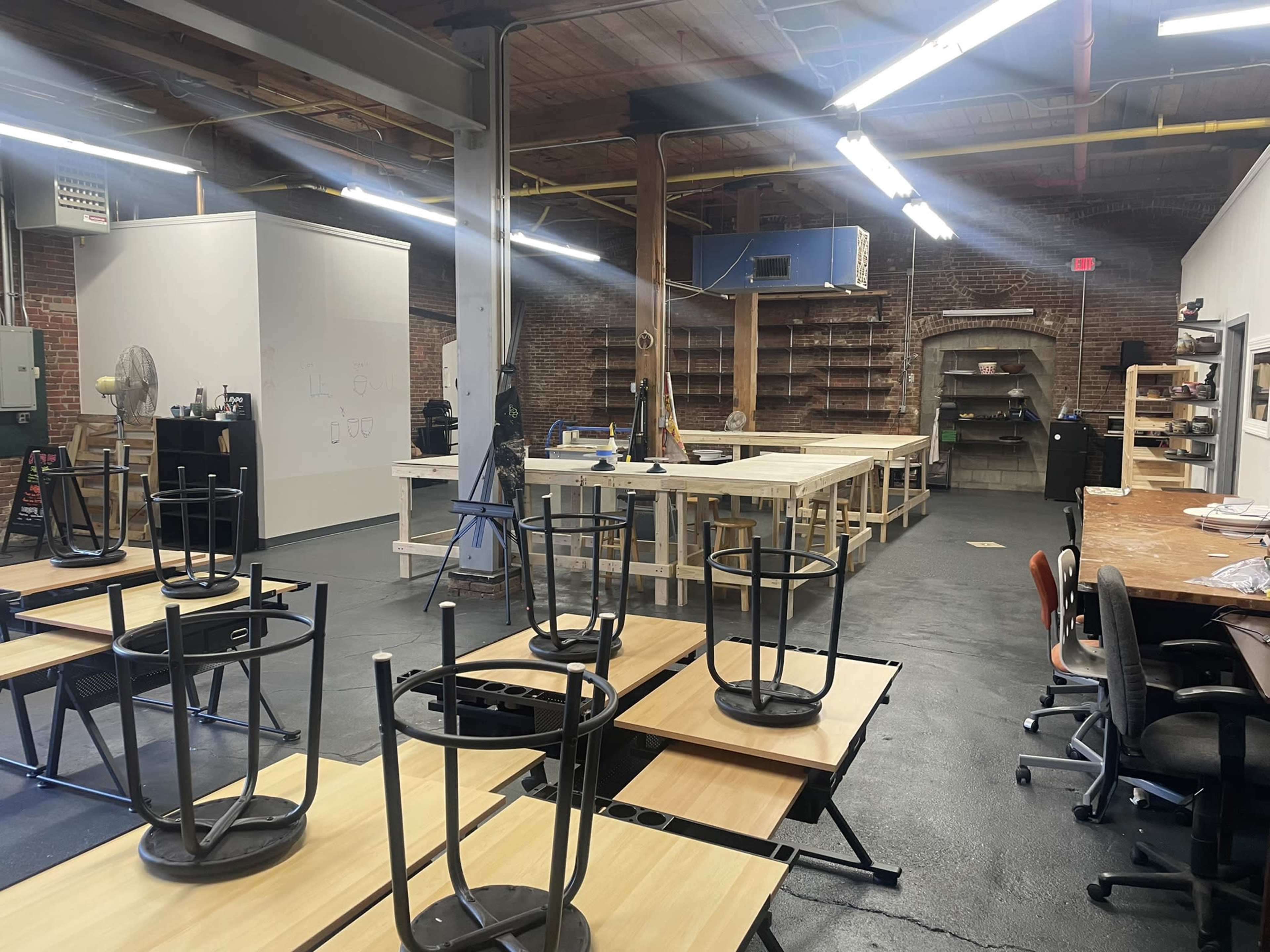 An empty room with overturned chairs and tables, wooden worktables, and shelves against the brick walls.