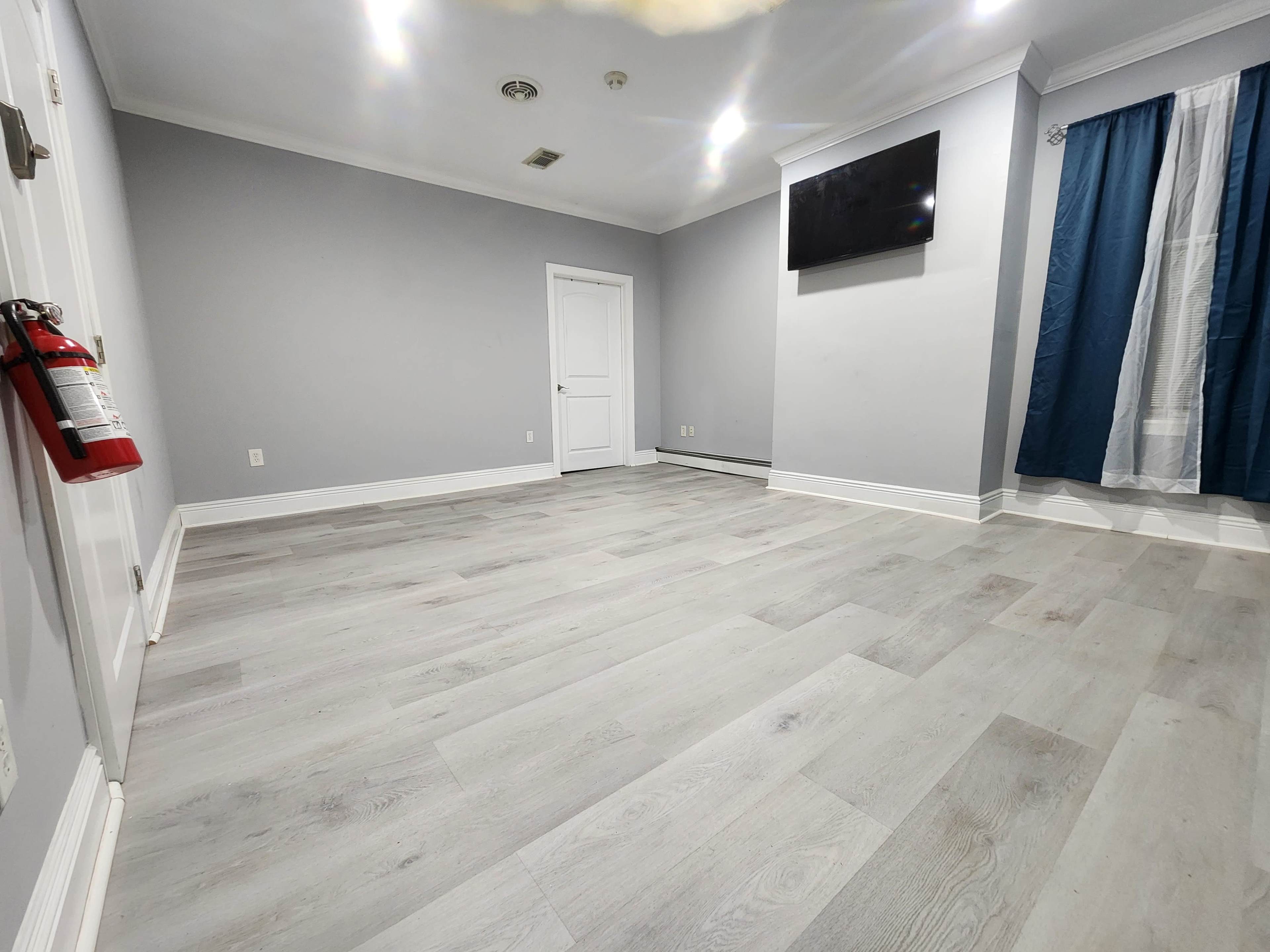 A sparse room with light gray walls, a TV mounted on one wall, and light wood flooring.