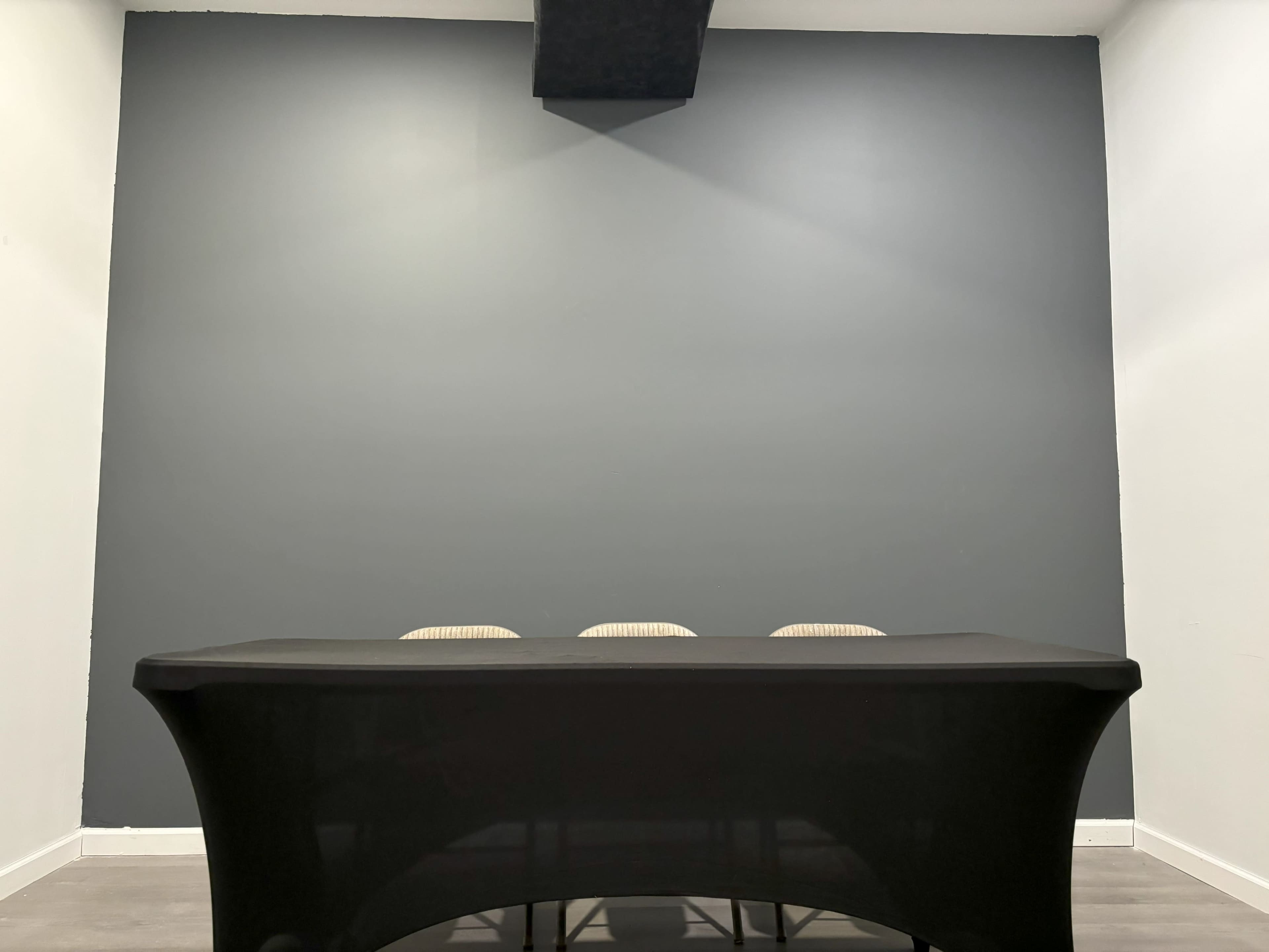 A black table with three chairs is positioned against a dark gray wall in a plain room.