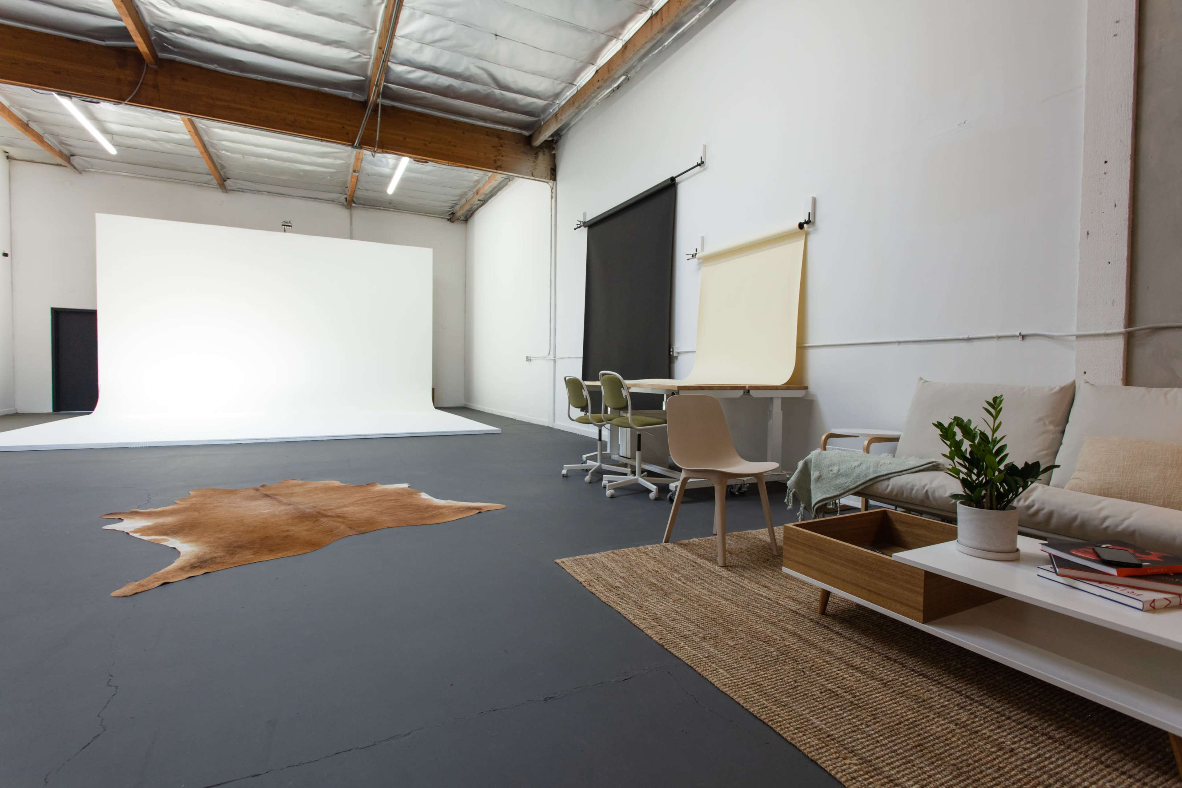 The image shows a spacious, modern studio featuring a blank white backdrop, a seating area with a coffee table, and several workstations.