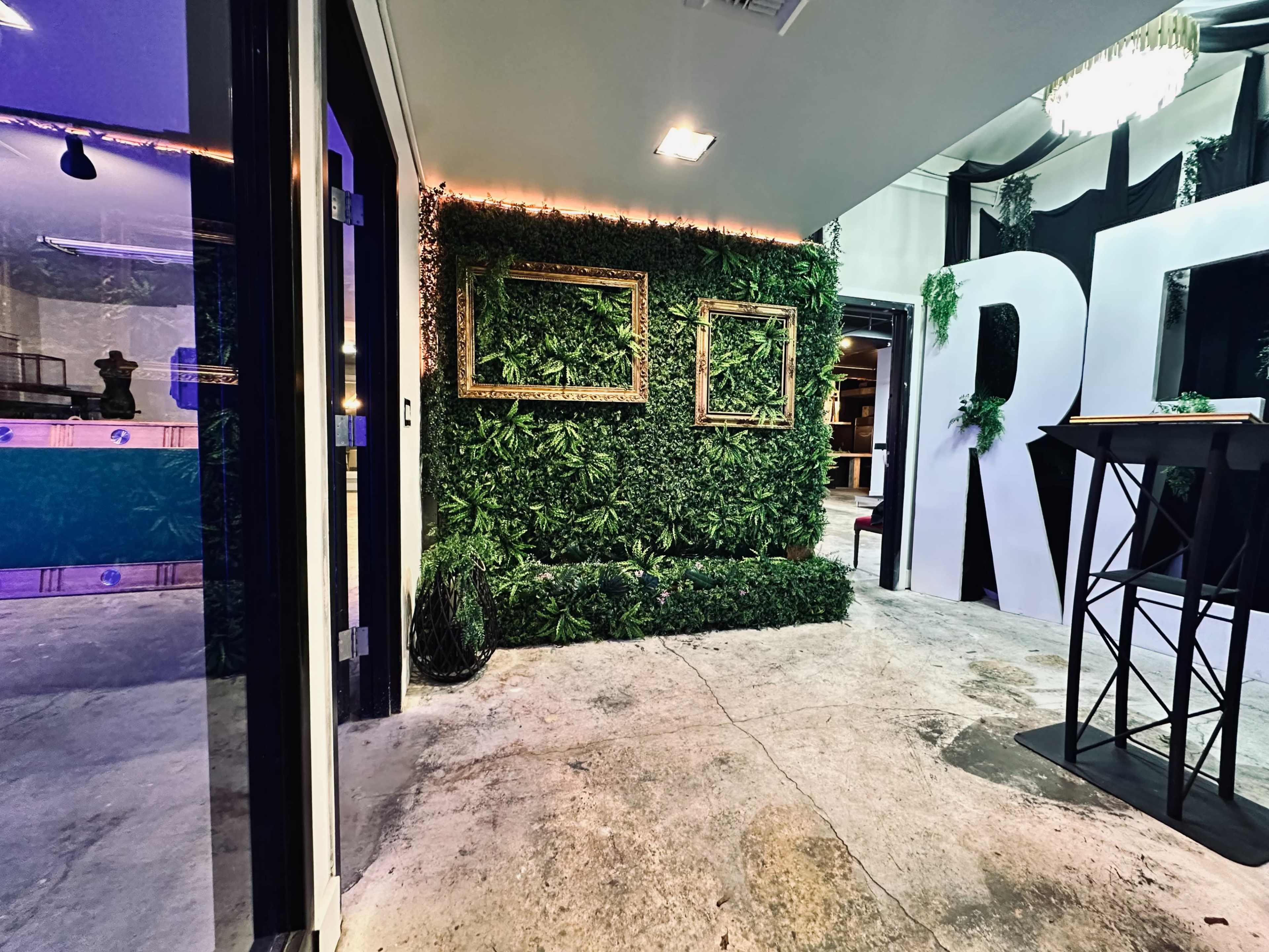 The image shows a modern interior space with a green vertical garden section, framed wall sections, and large letter decorations.