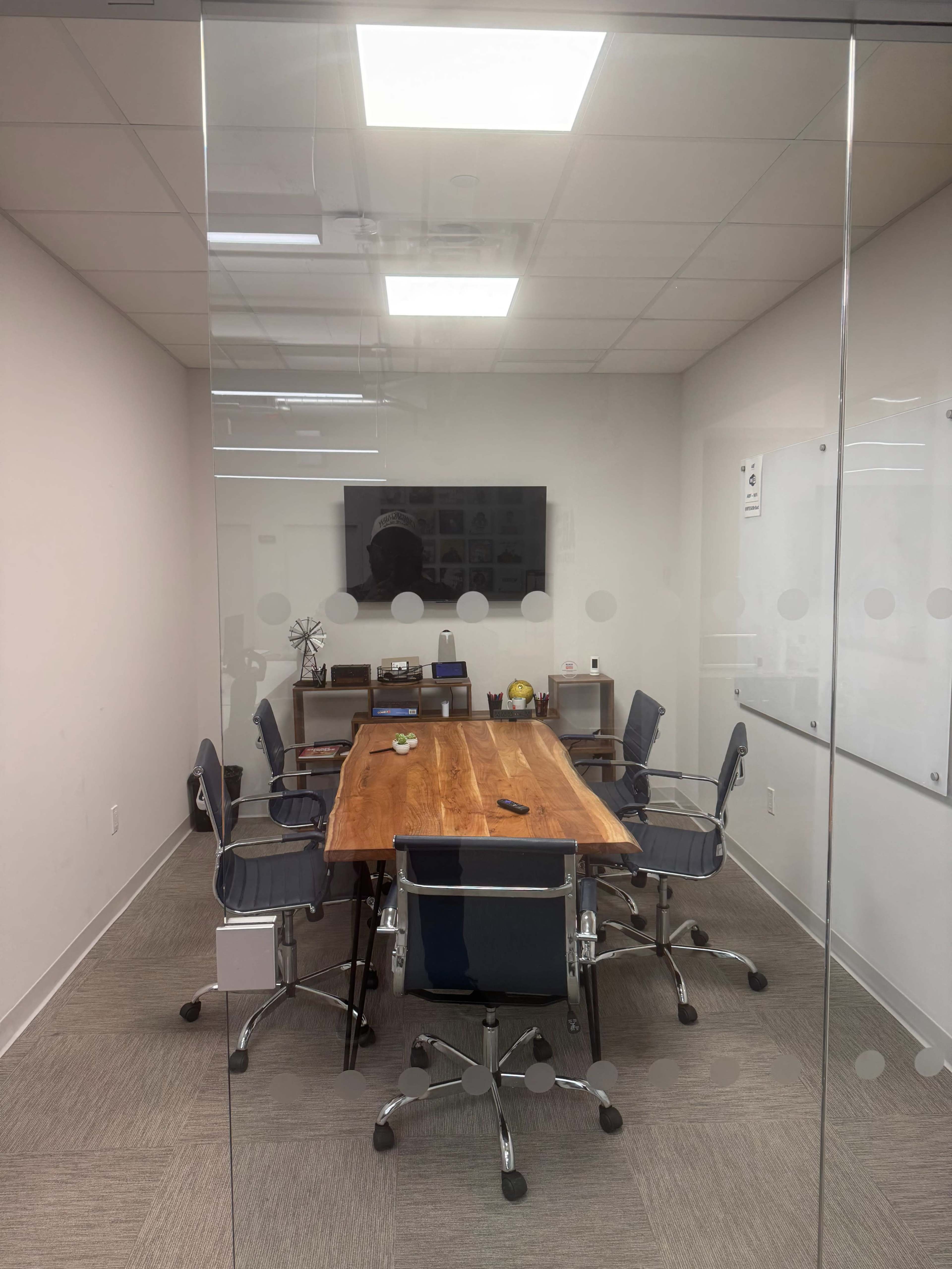 The image shows a conference room with a large wooden table surrounded by several chairs, a television mounted on the wall, and a whiteboard.