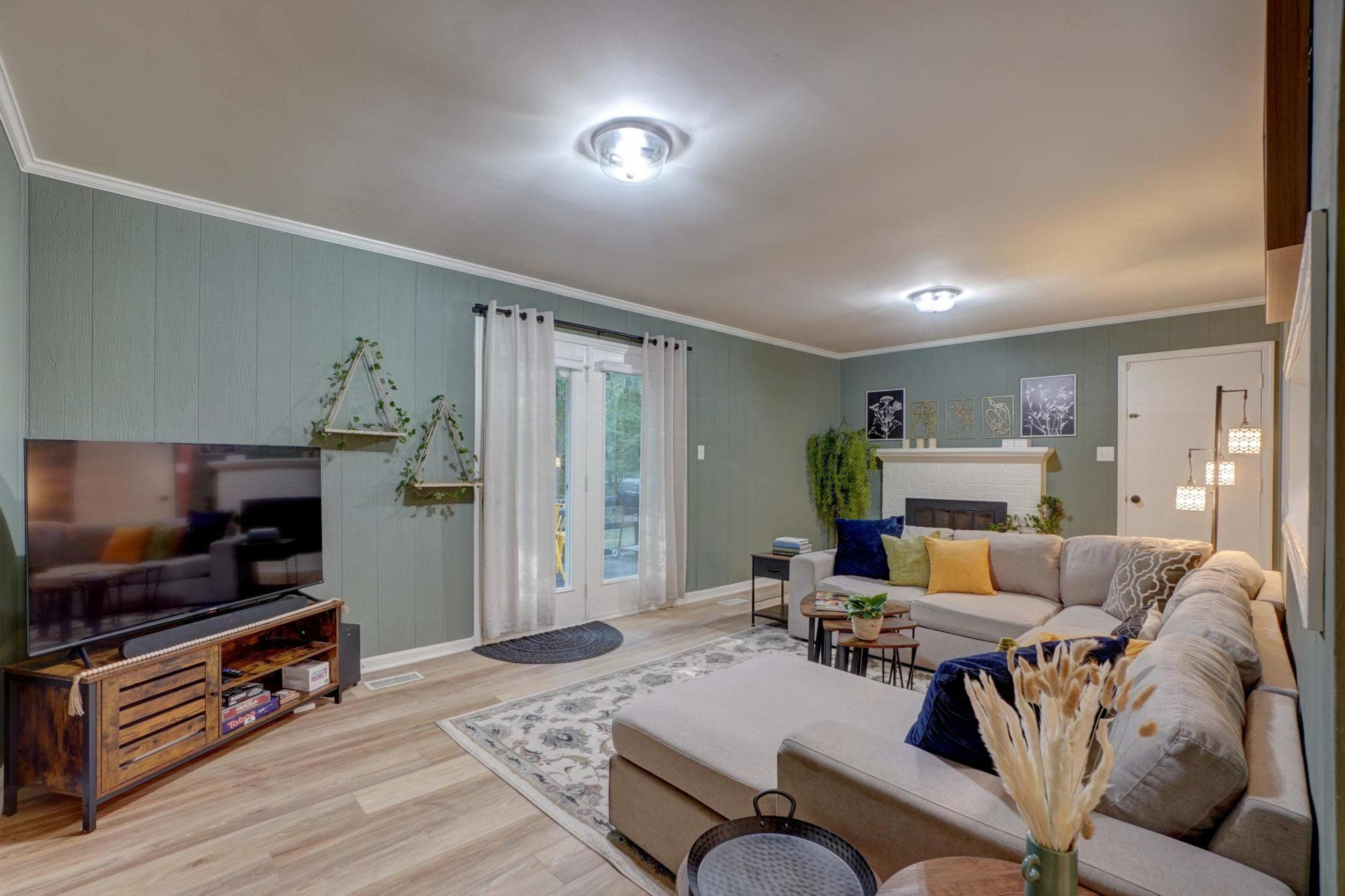 The image shows a well-lit living room with a beige sectional sofa, a television on a wooden stand, and a door leading to an outdoor area.