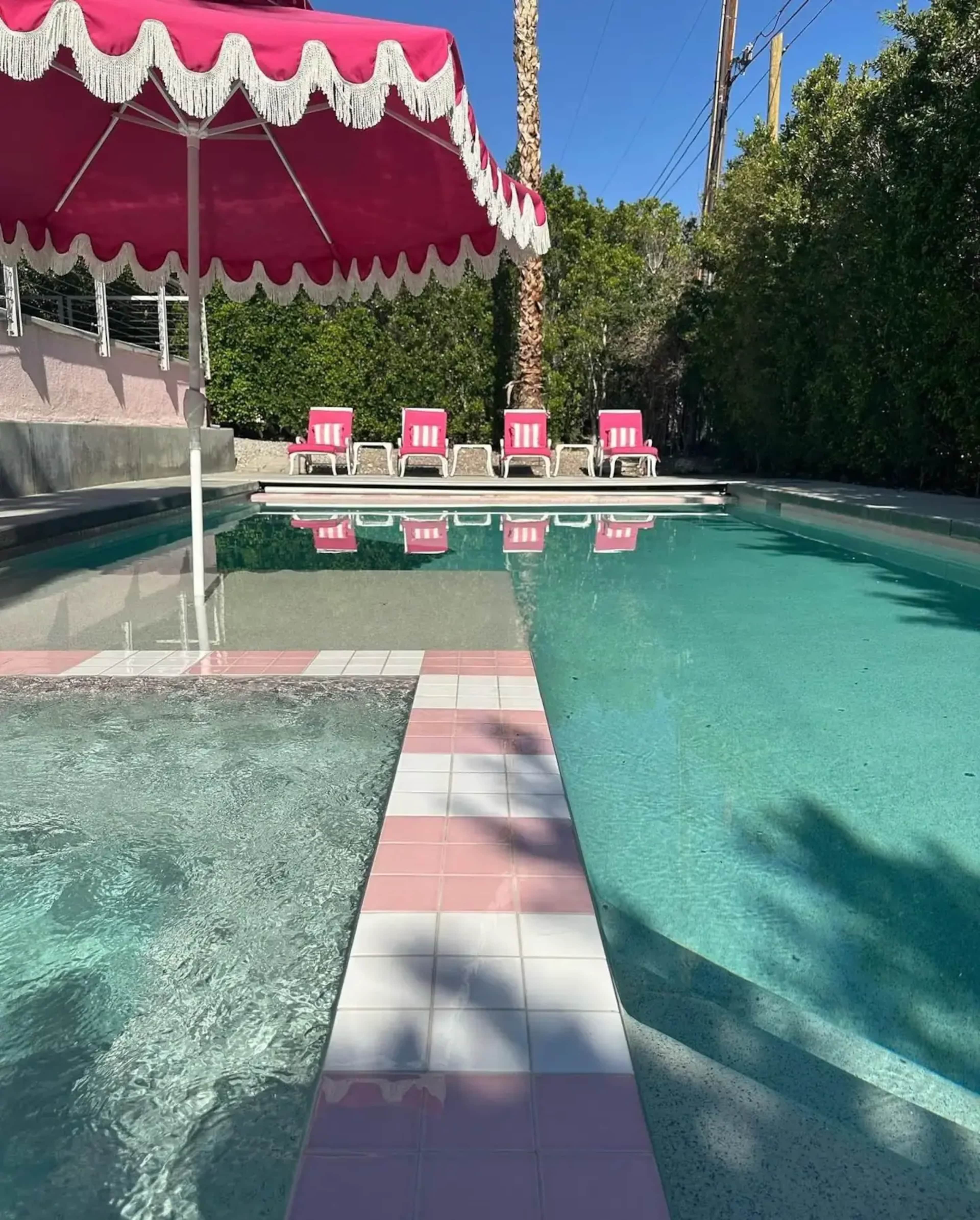 A bright pool area features pink-and-white striped lounge chairs and a large pink umbrella beside the water.