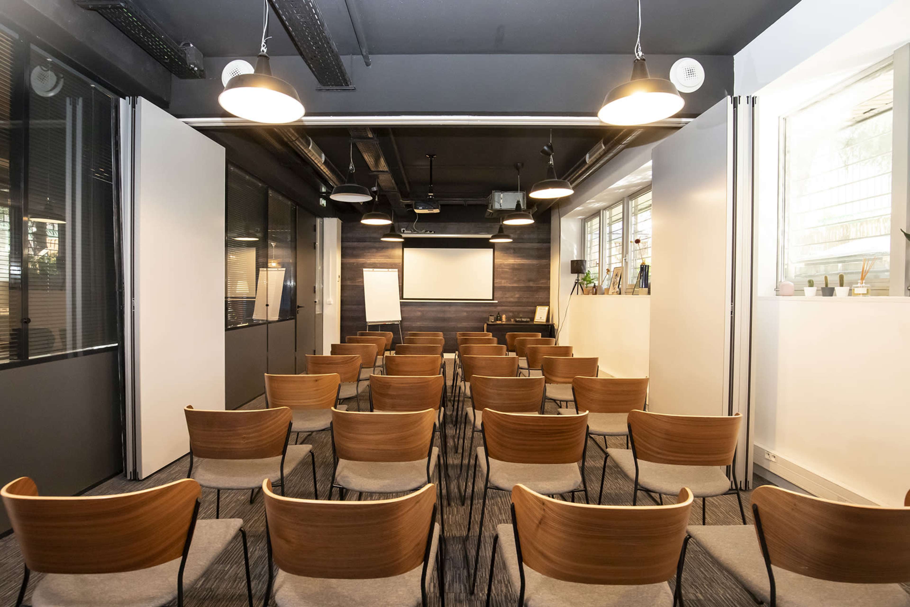 A modern conference room set up with rows of chairs facing a projection screen on a dark wooden wall.