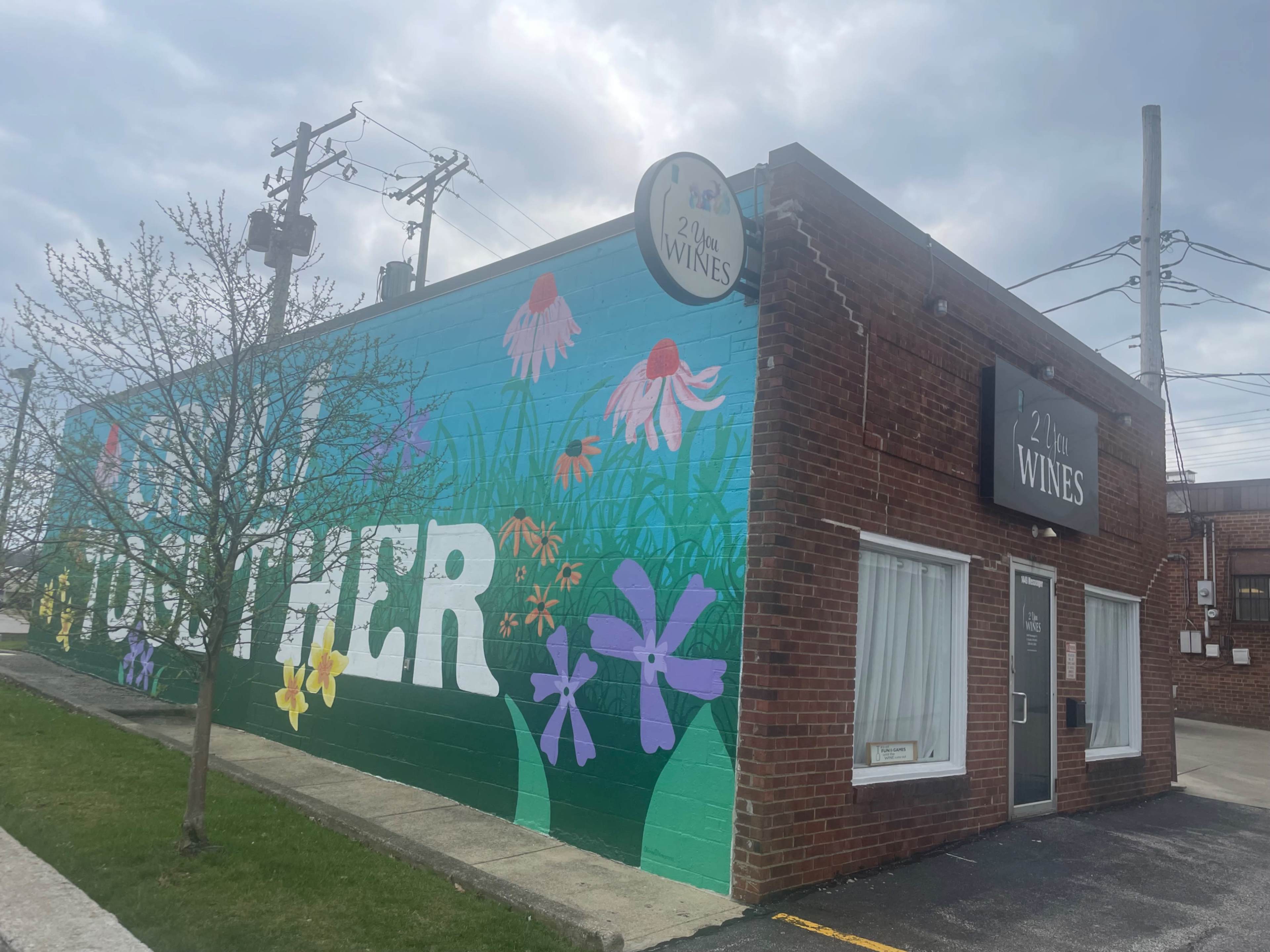 The image shows a brick building with a colorful mural featuring flowers and the word "TOGETHER" on its exterior, along with a sign indicating it is a wine shop.