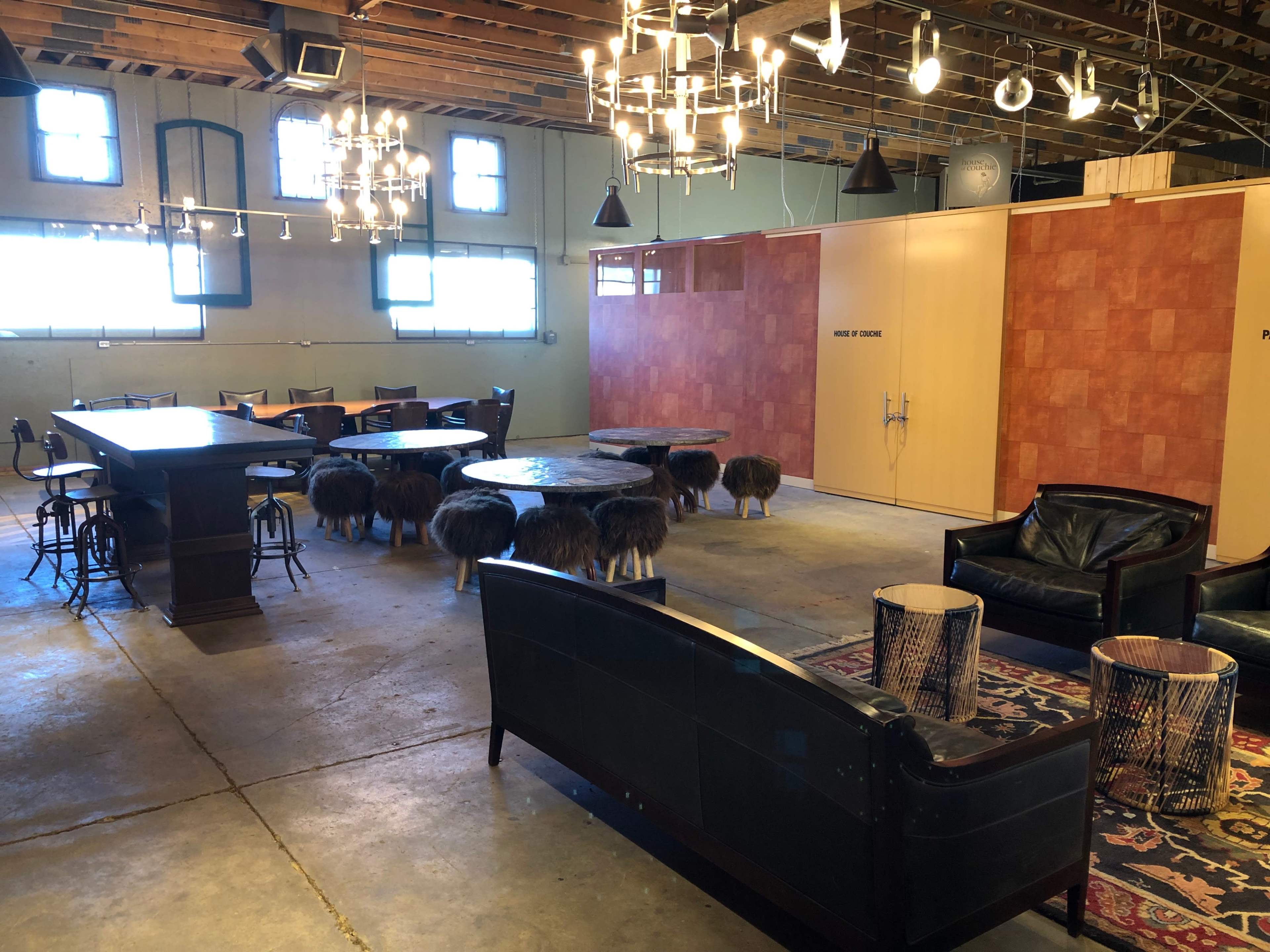 A spacious room with a large wooden table, various seating areas, and several animal-shaped stools arranged on a concrete floor.