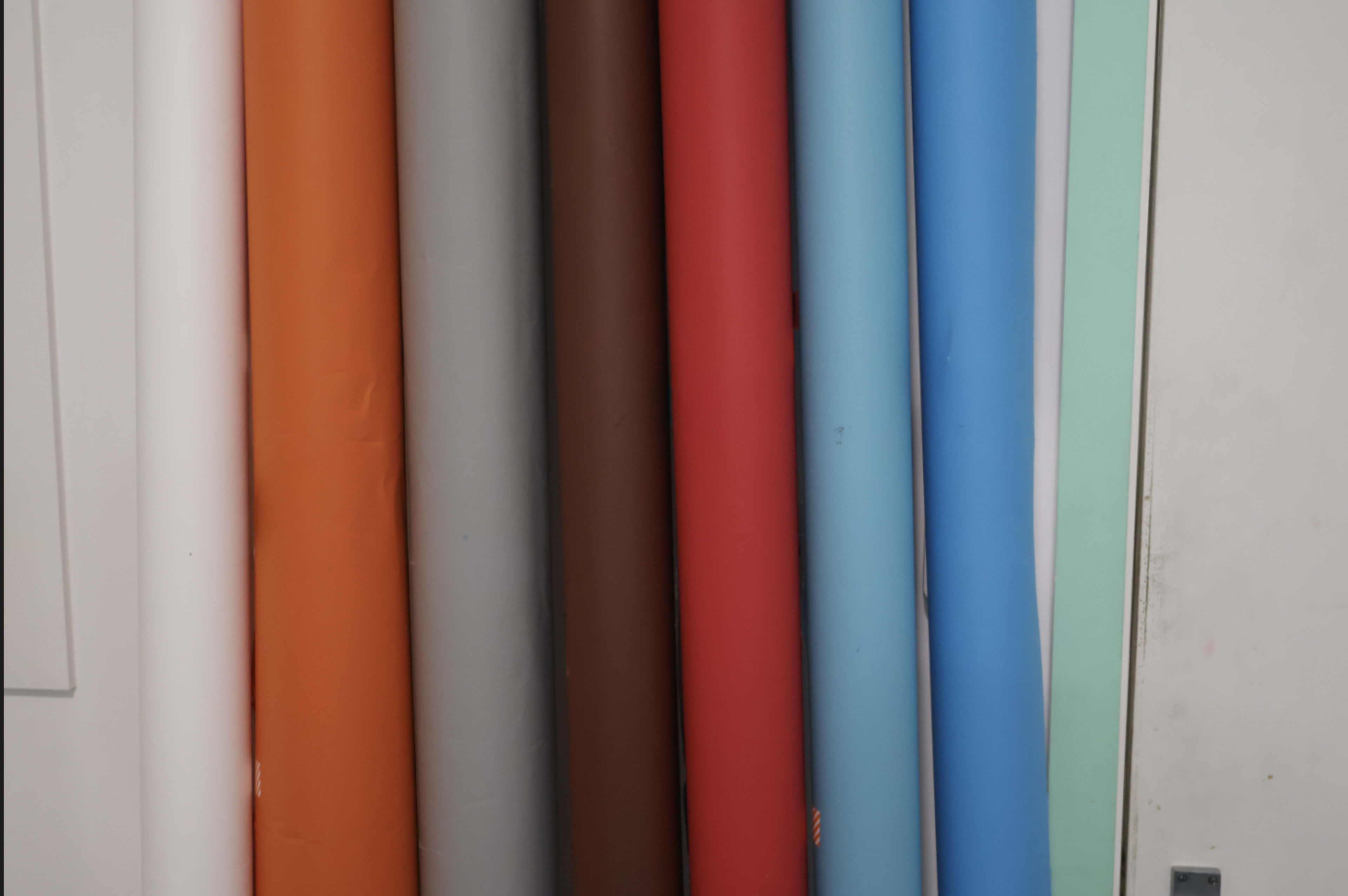 The image shows a collection of rolled paper in various colors lined up against a wall.