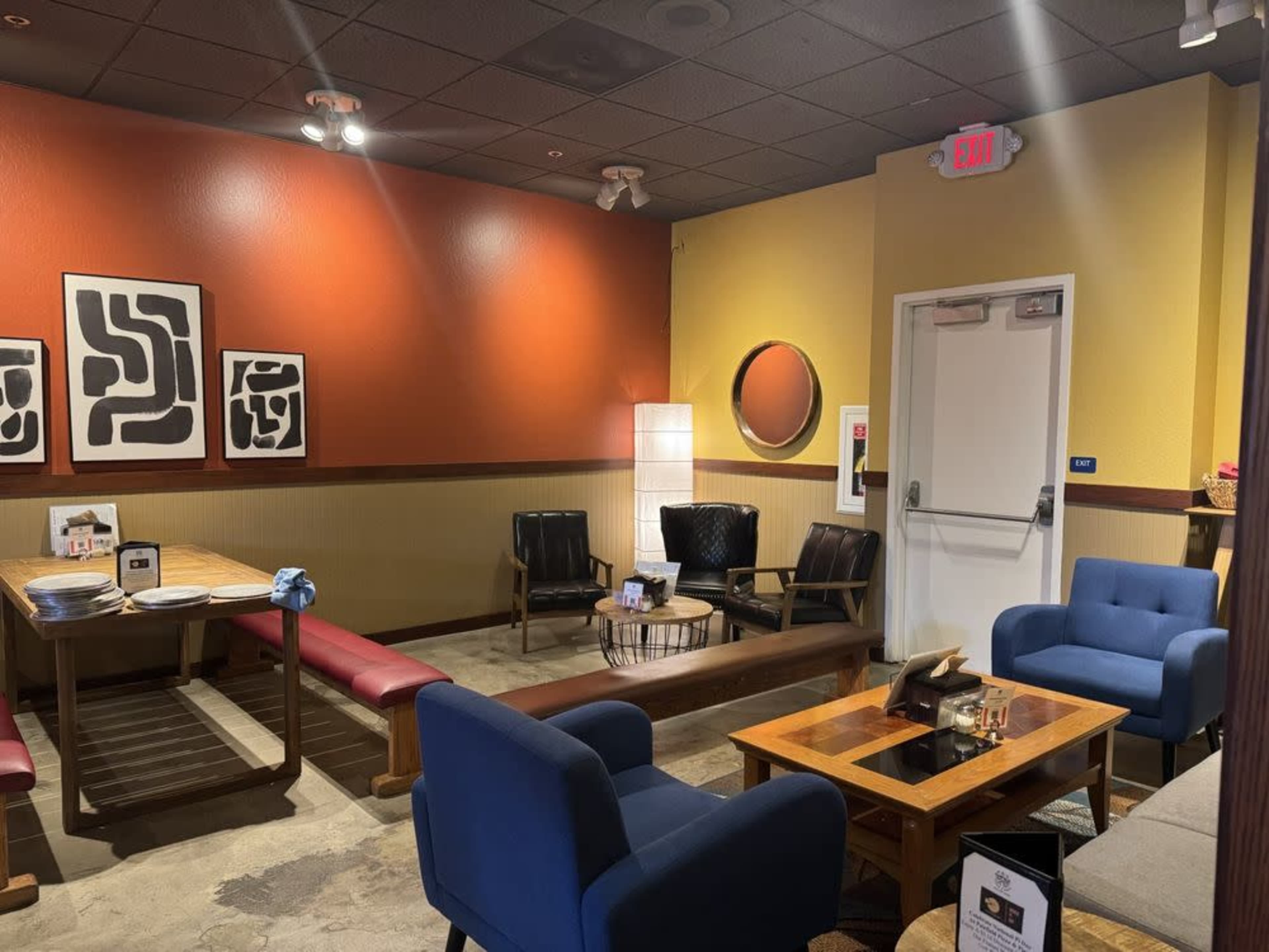 The image displays a cozy room featuring a mix of seating options, artwork on the walls, and a decorative light fixture.