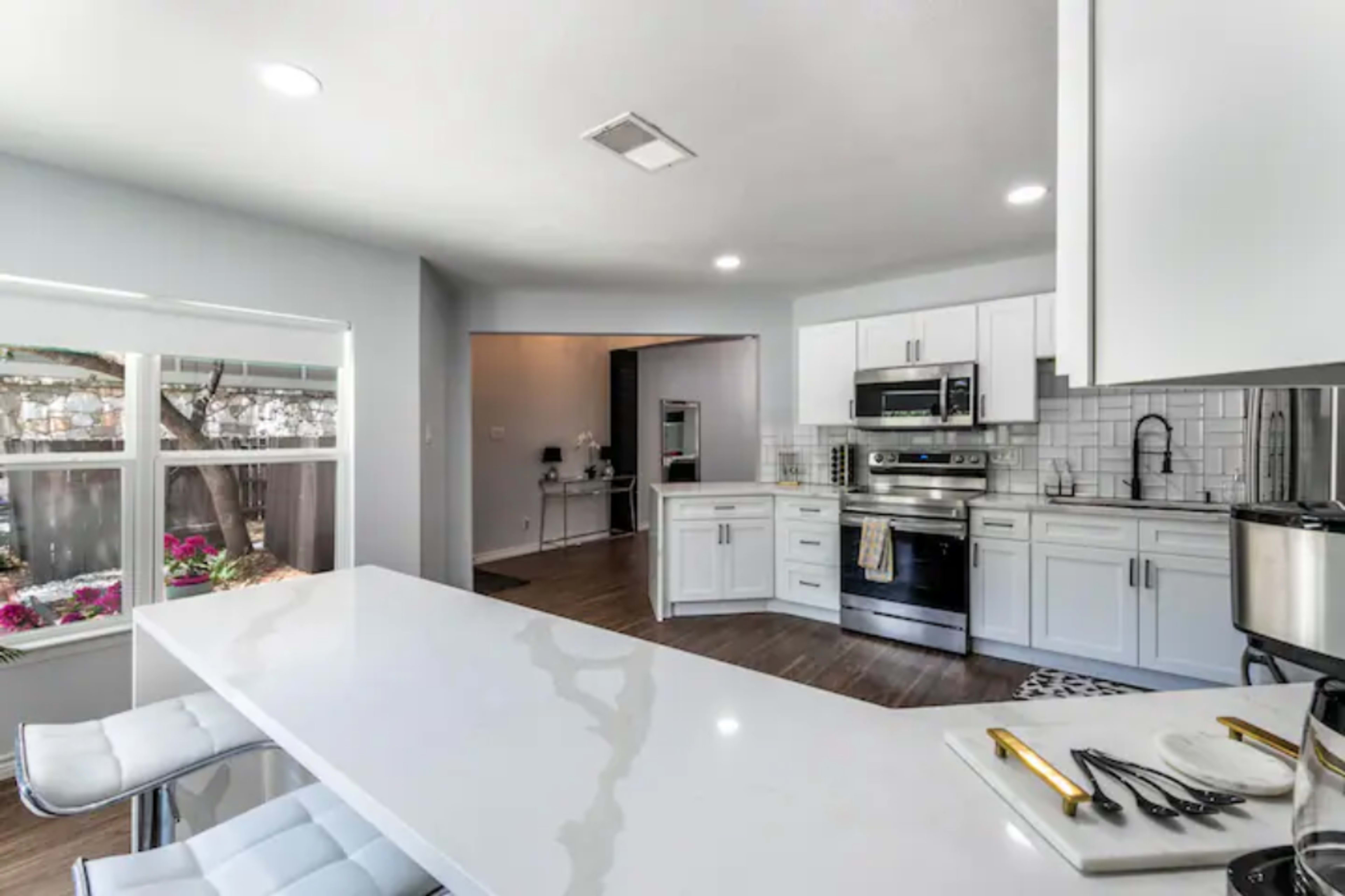 A modern kitchen with white cabinetry, stainless steel appliances, and a large, white countertop with bar seating.
