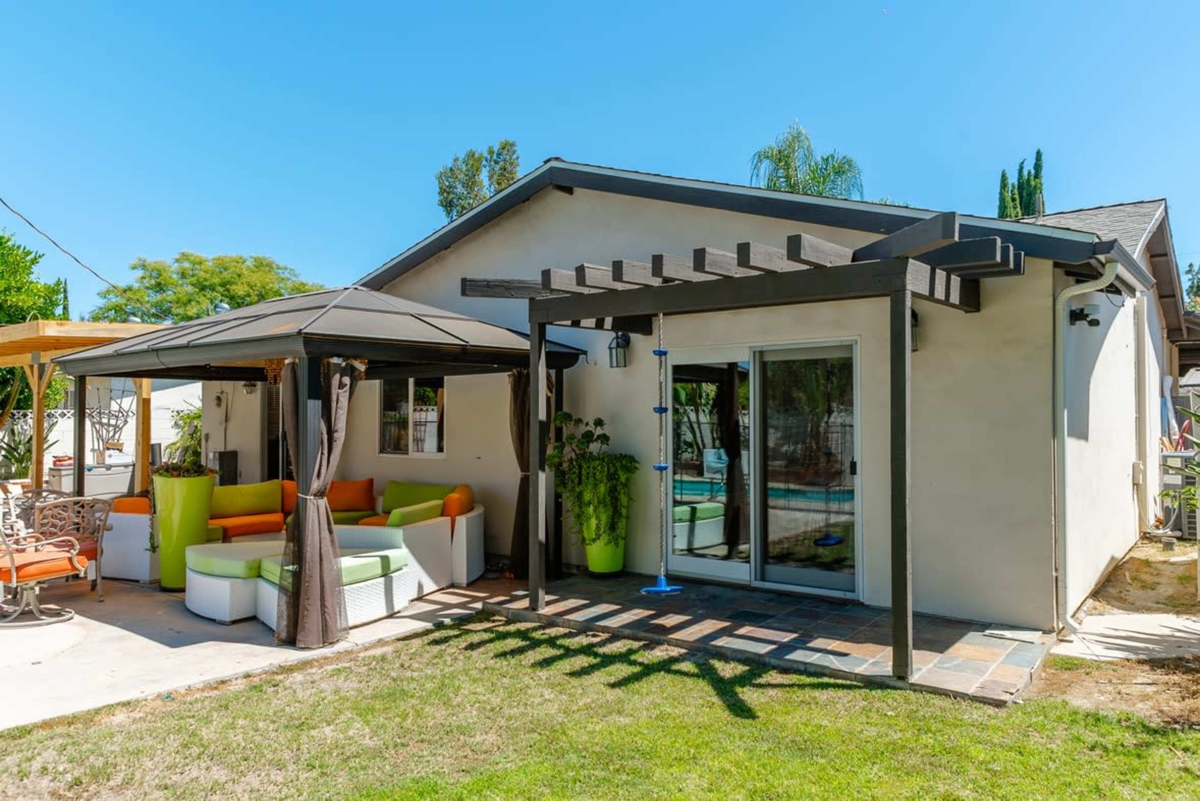 A modern backyard features a patio area with a gazebo and a seating arrangement next to a house.