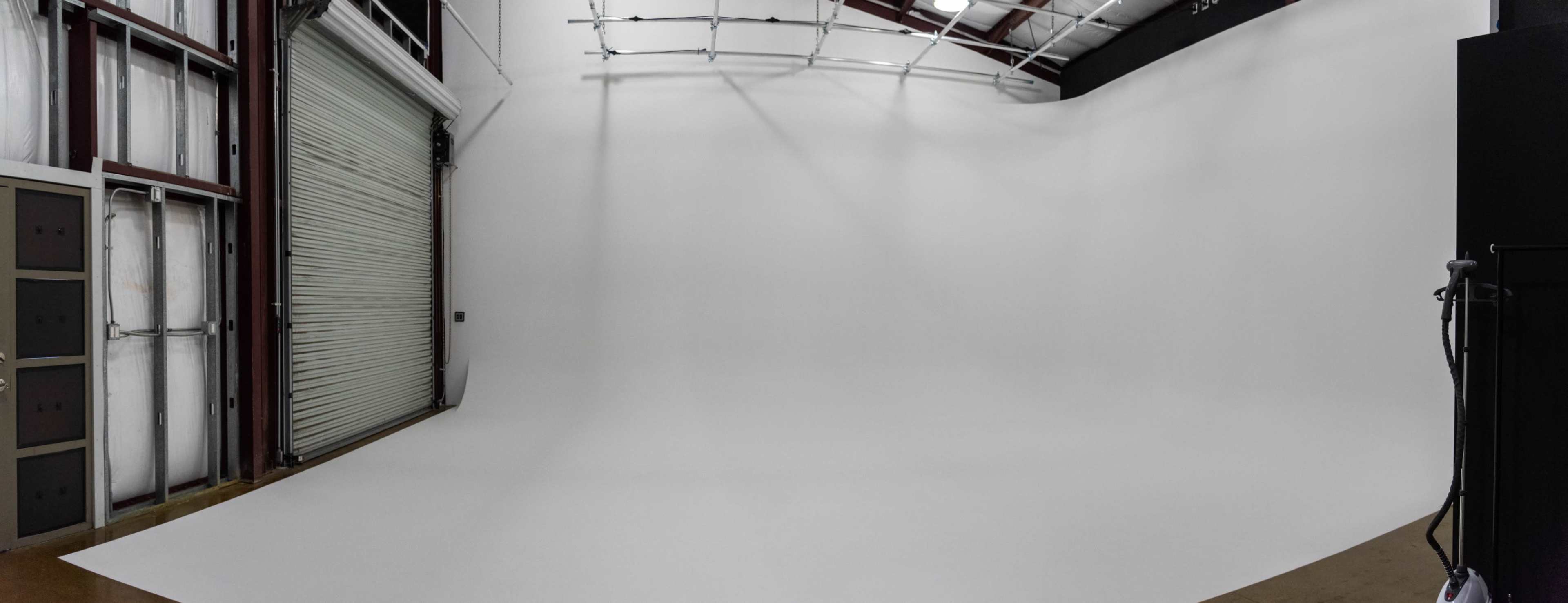 A spacious, empty studio with a seamless white backdrop and a large garage door.