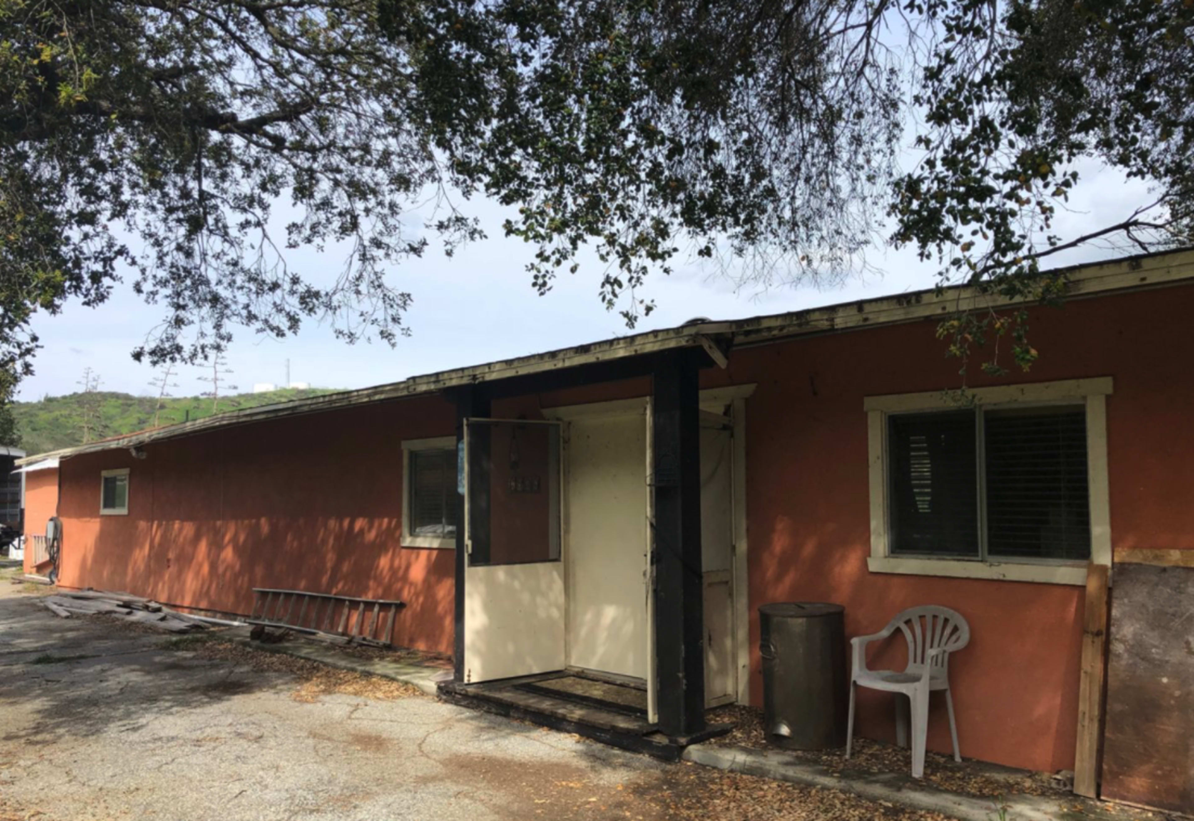 A single-story building with an orange exterior has an open door, and a white plastic chair is positioned outside.