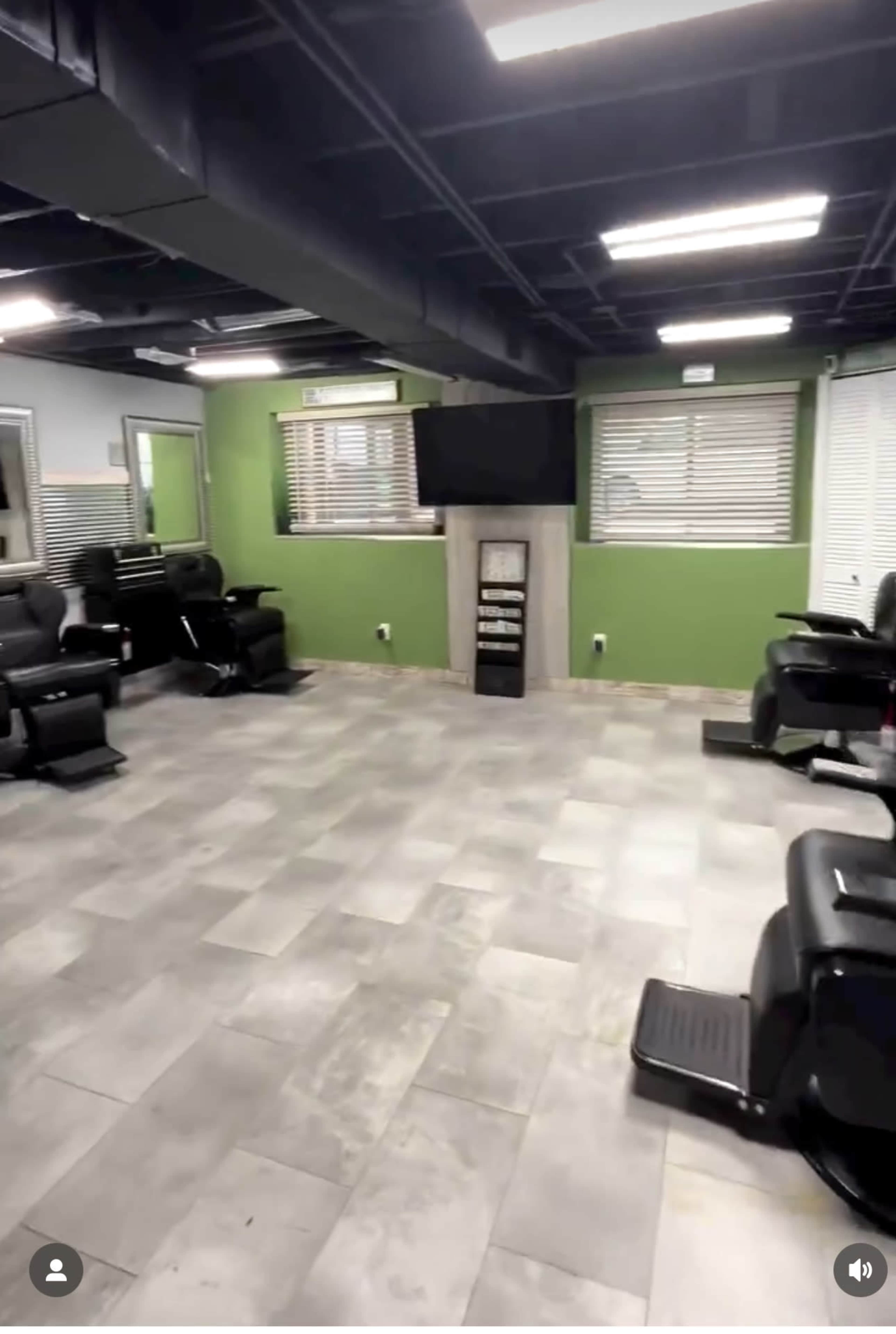 An empty hair salon with several styling chairs, a television mounted on the wall, and green-painted walls.