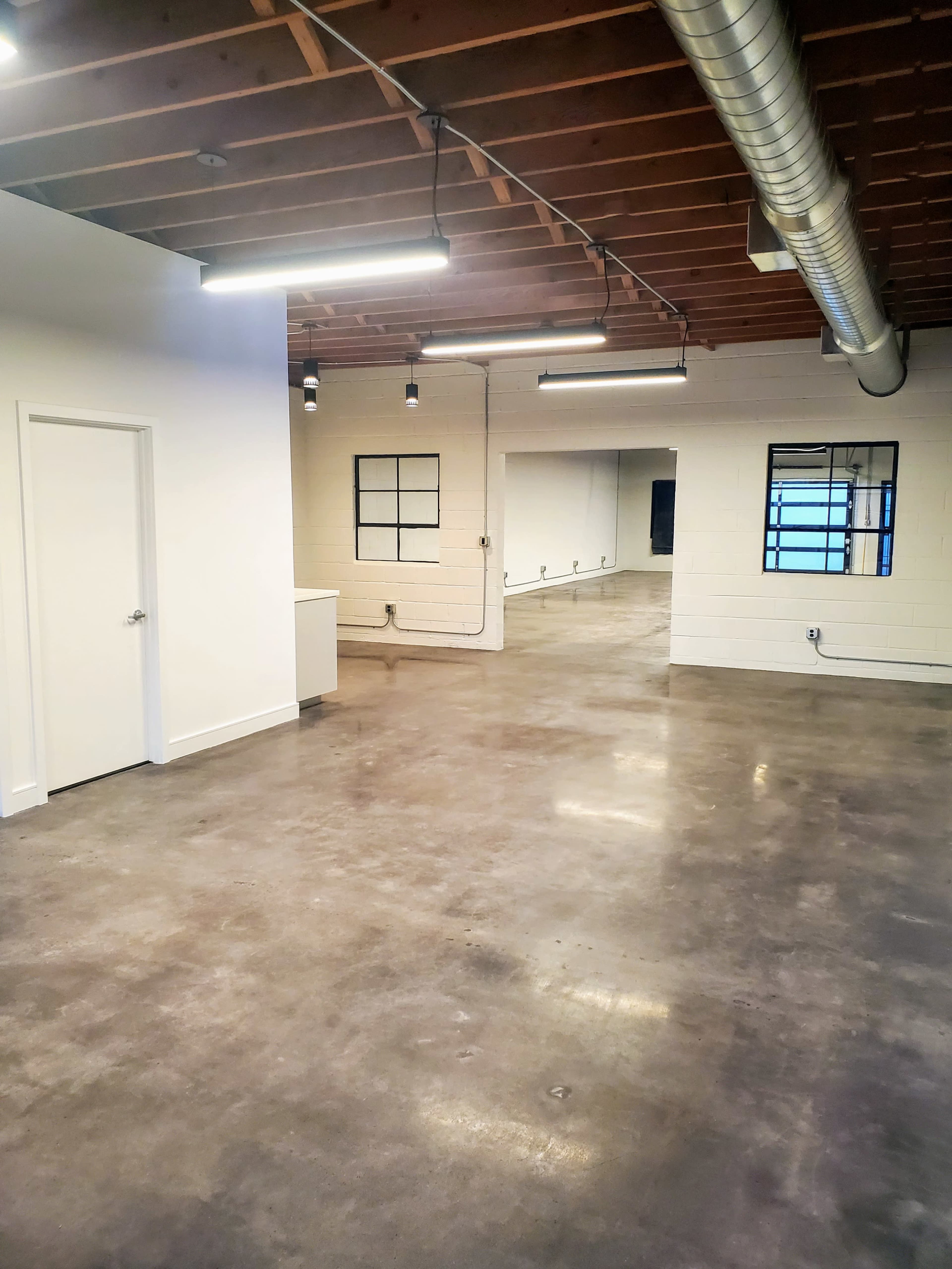 The image shows a spacious, modern office interior with polished concrete floors, exposed wooden beams, and large windows.