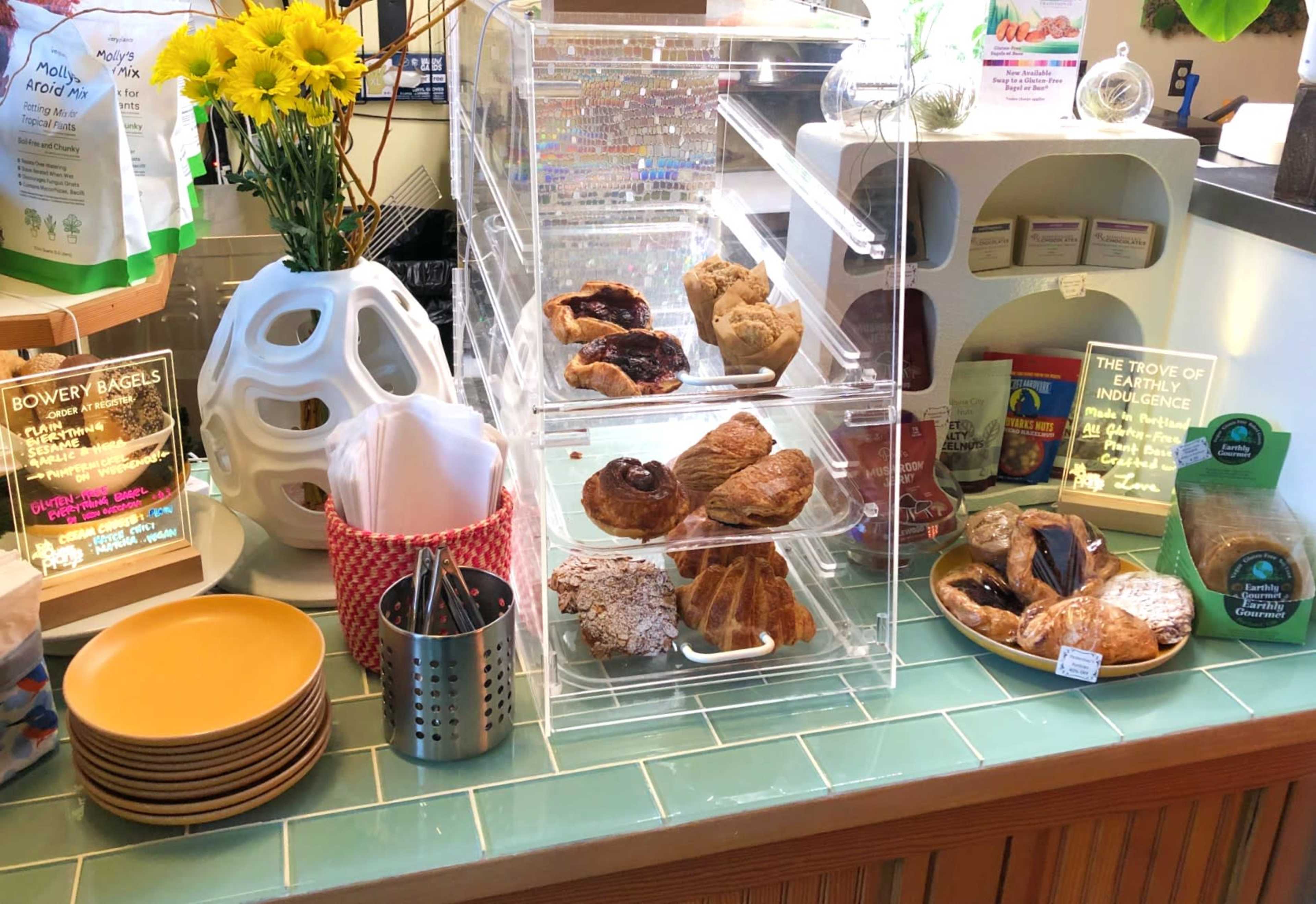 A display of assorted baked goods, including croissants and pastries, is arranged in clear containers on a countertop beside a vase of flowers and various condiments.