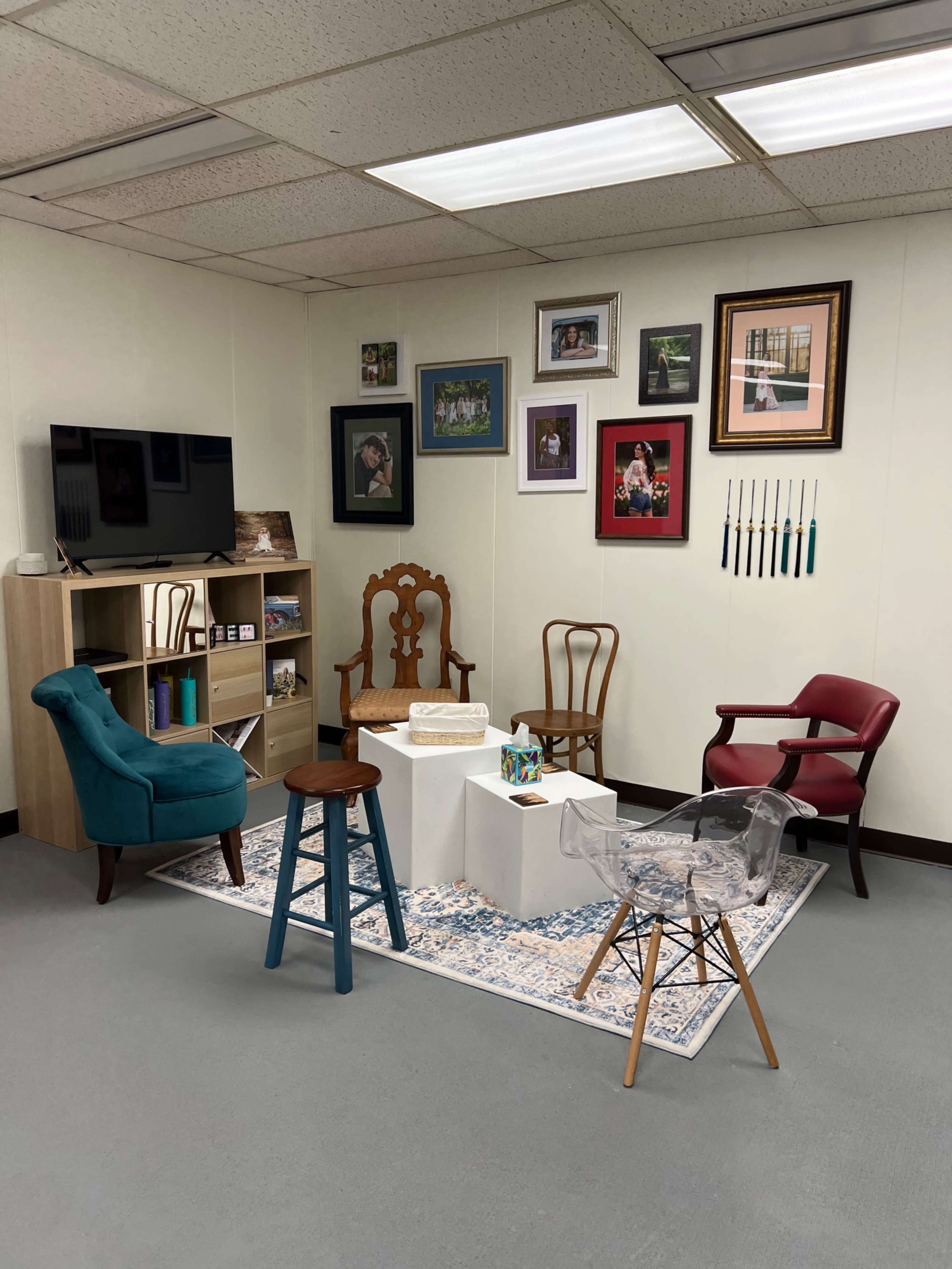 The image shows a cozy waiting area with a small table, various chairs, and a shelf with photos displayed on the walls.