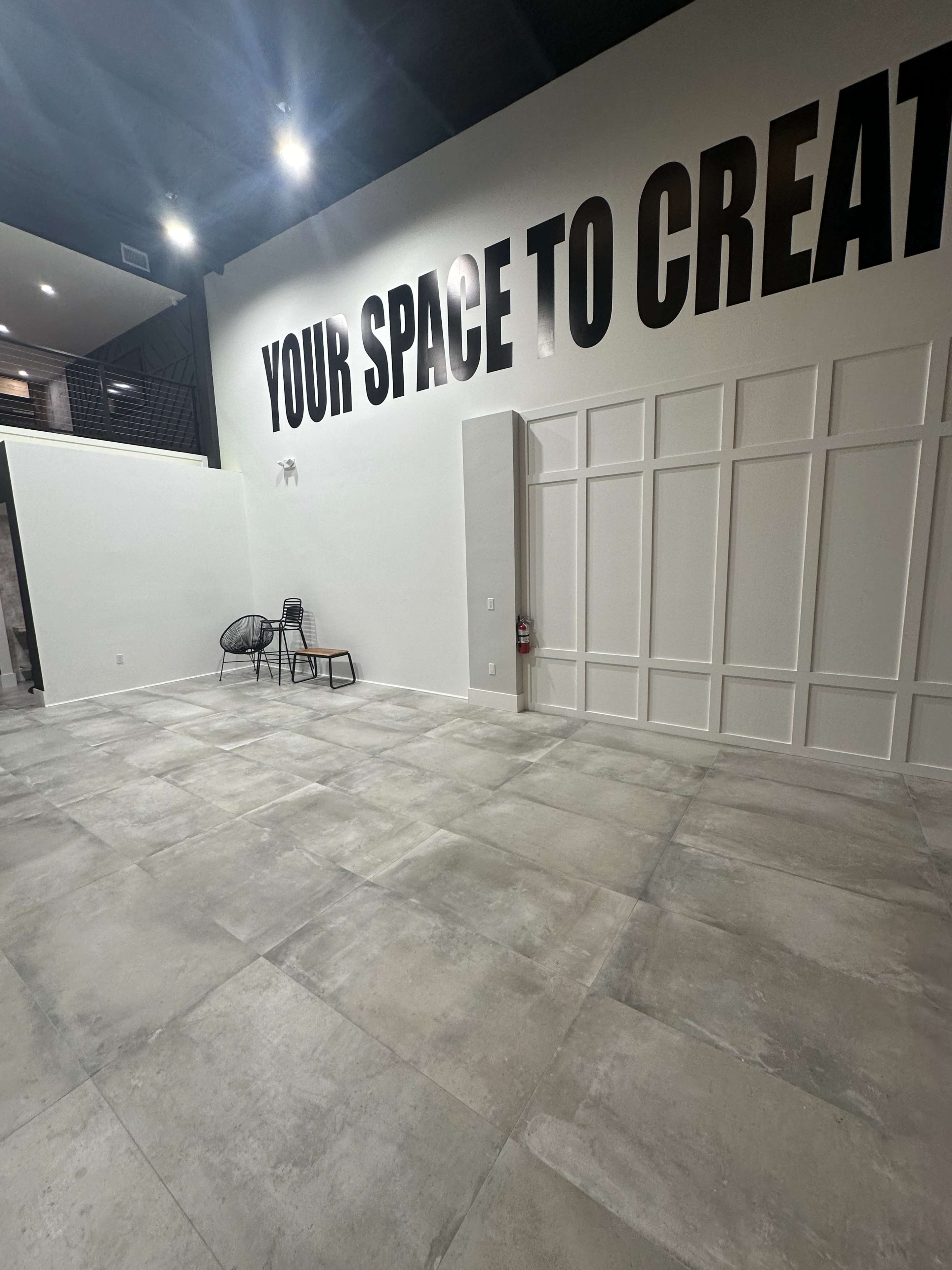 A spacious, empty room with gray tile flooring and a large wall featuring the words "YOUR SPACE TO CREATE."