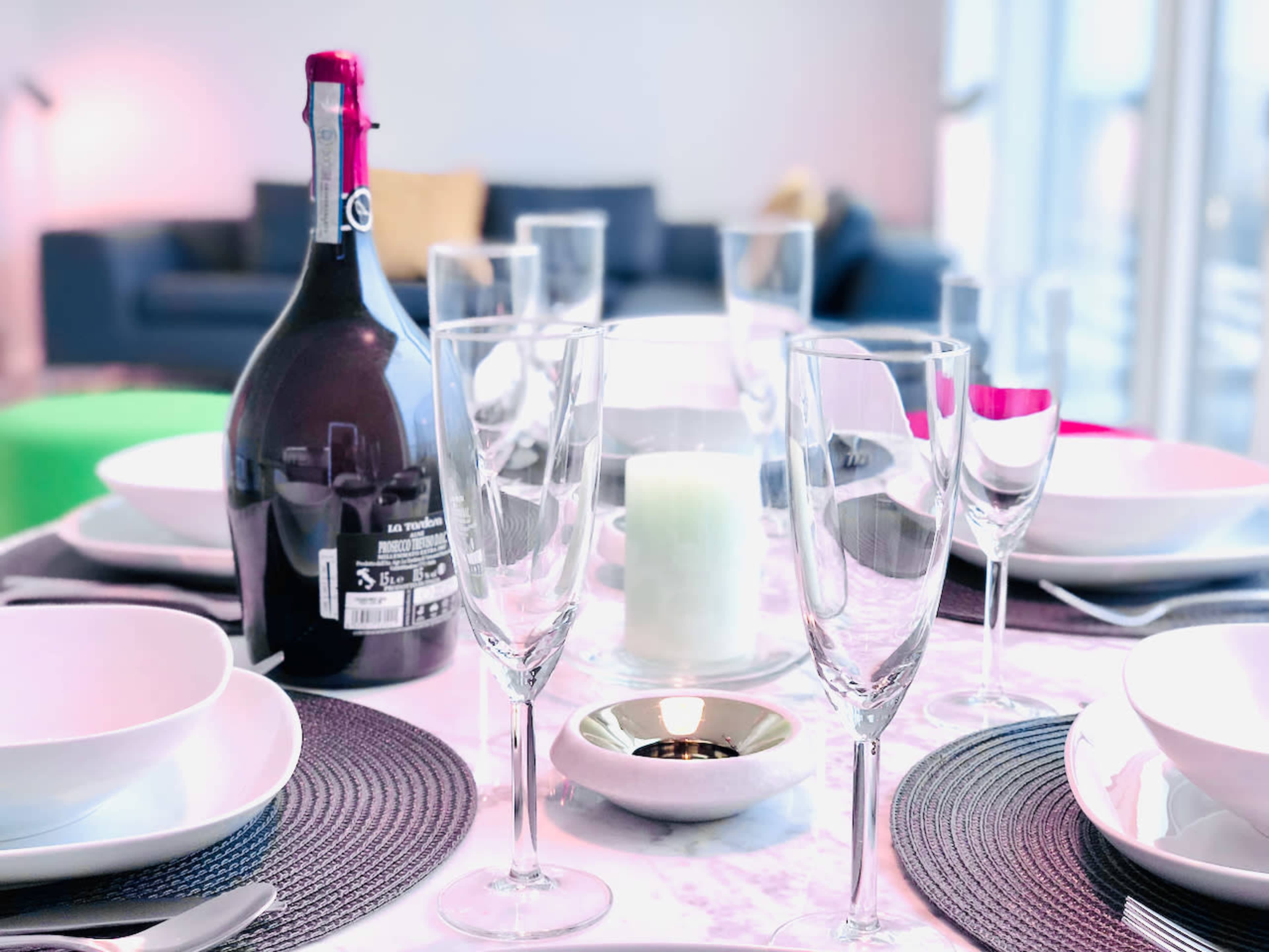 A dining table is set with multiple glassware, plates, and a bottle of wine, accompanied by a lit candle in the center.
