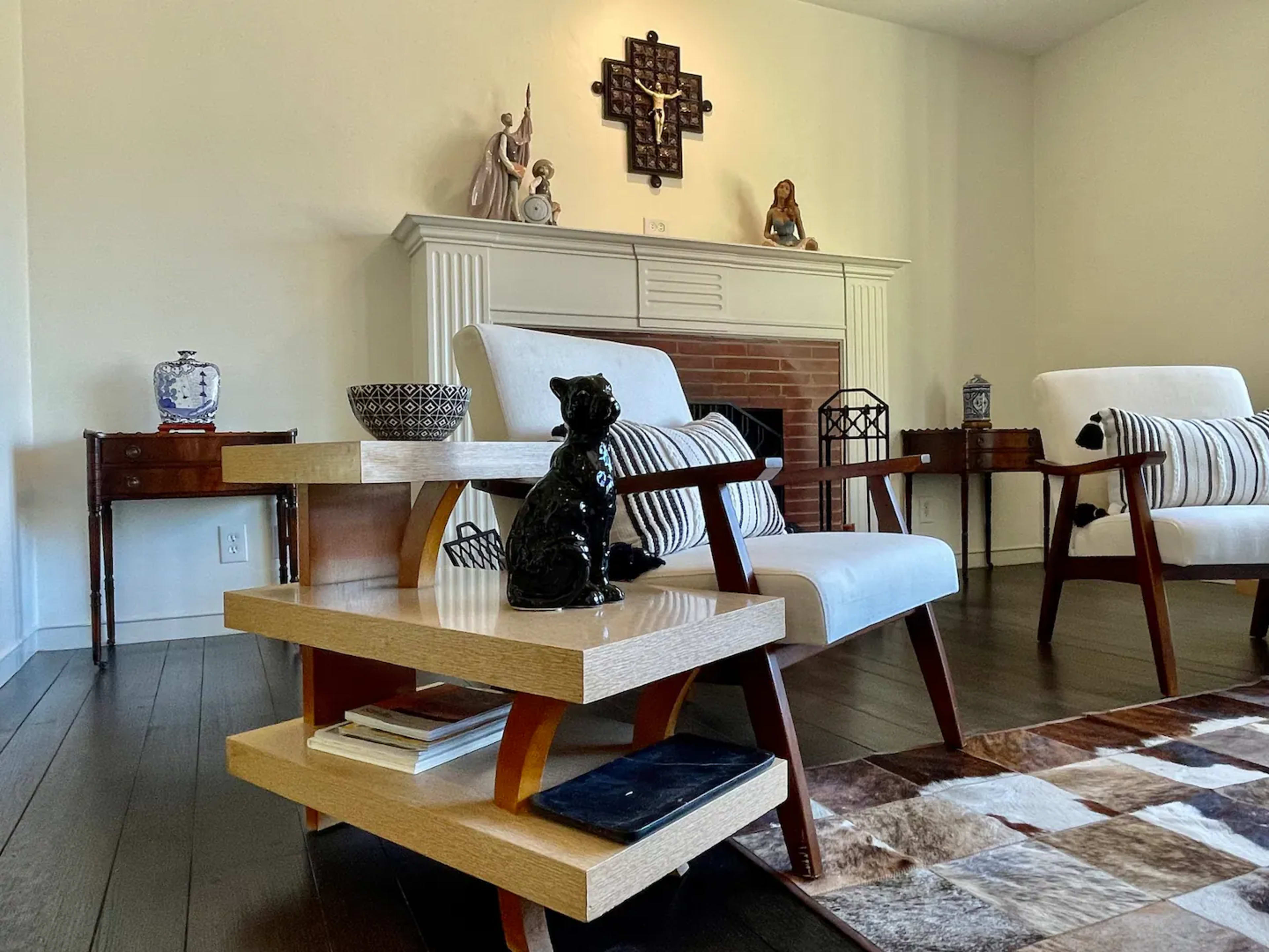 A living room with two modern chairs, a wooden coffee table featuring a decorative black dog statue, and a fireplace adorned with various objects.