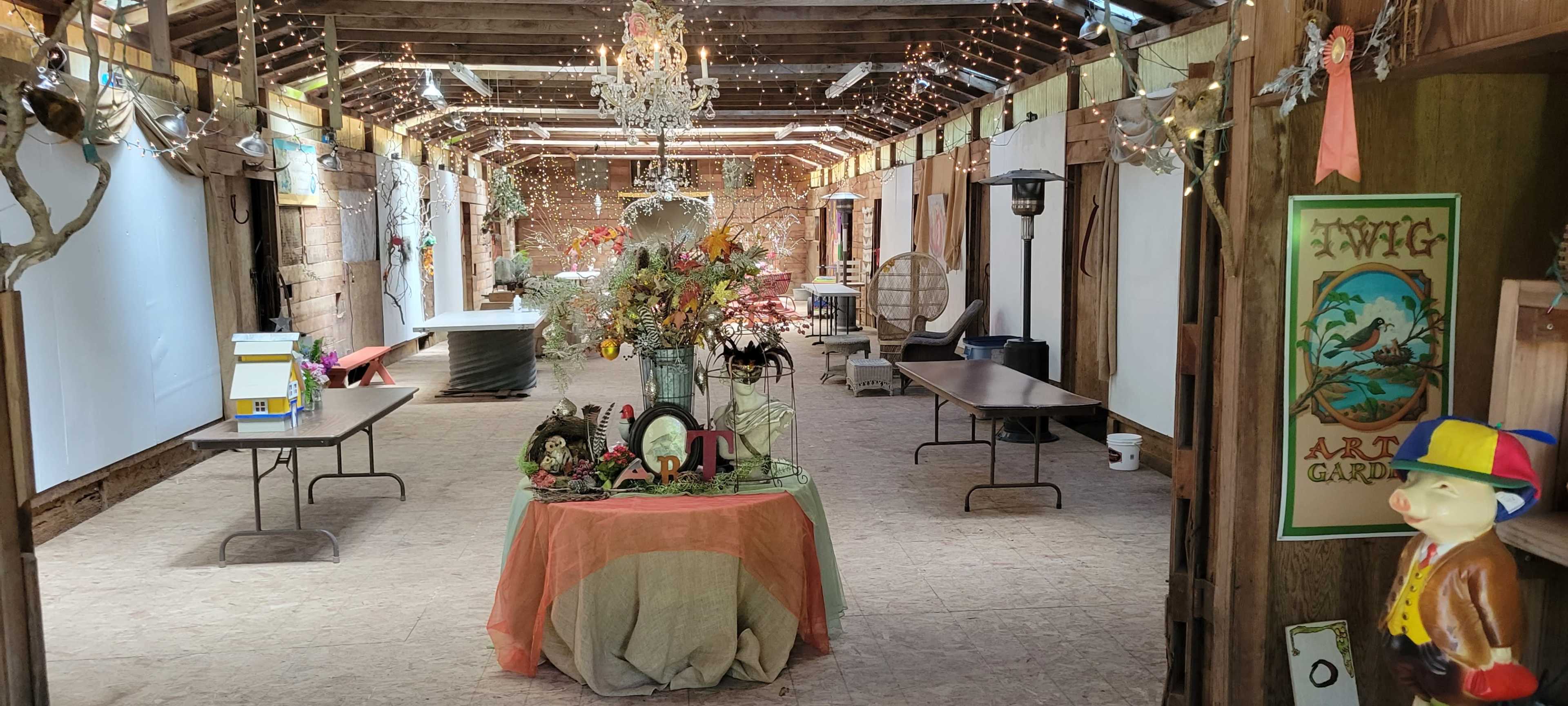A spacious indoor venue adorned with string lights, featuring tables, decor, and a centerpiece of flowers and figurines.