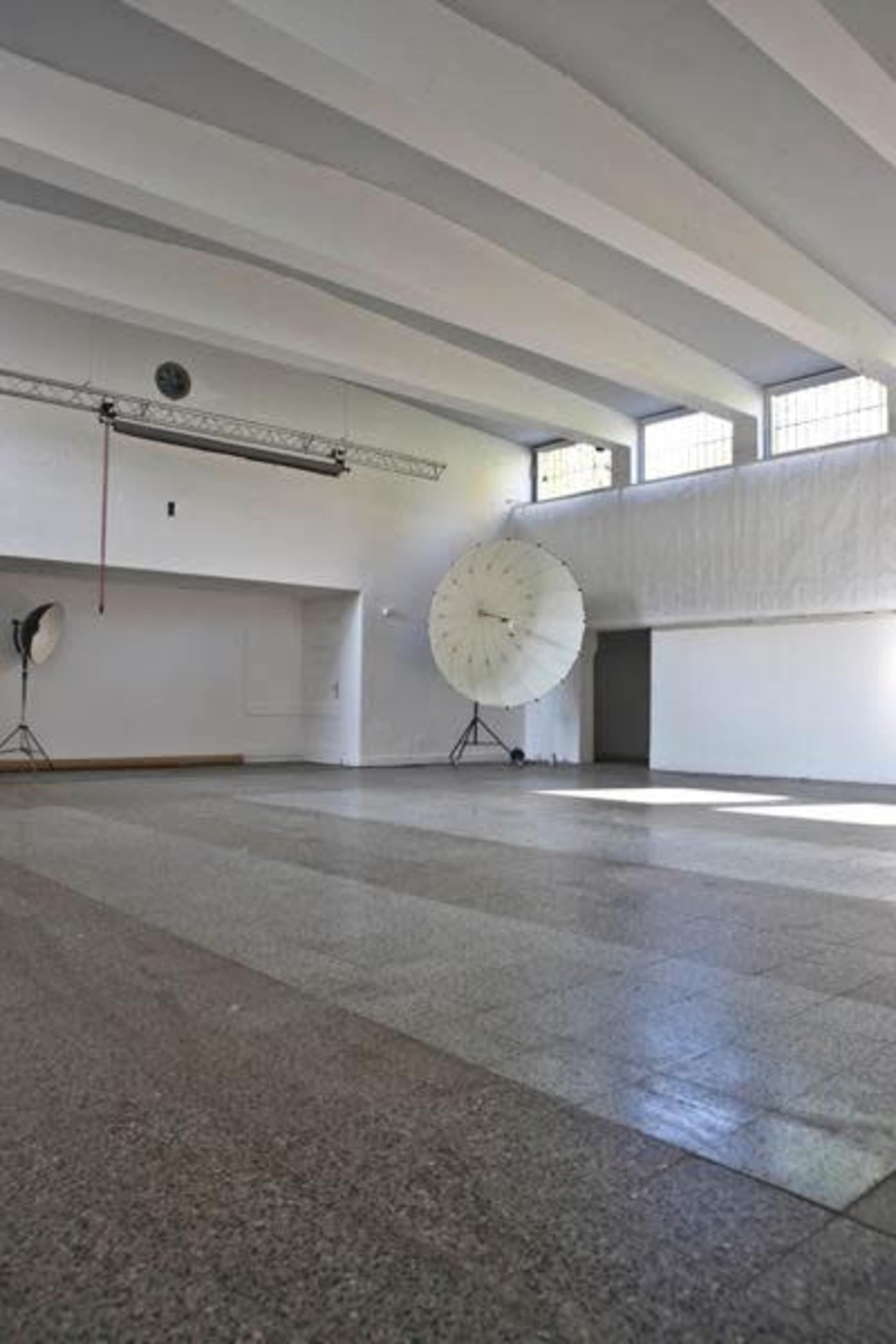 A spacious, well-lit studio with a polished floor, large windows, and two softboxes positioned on either side.
