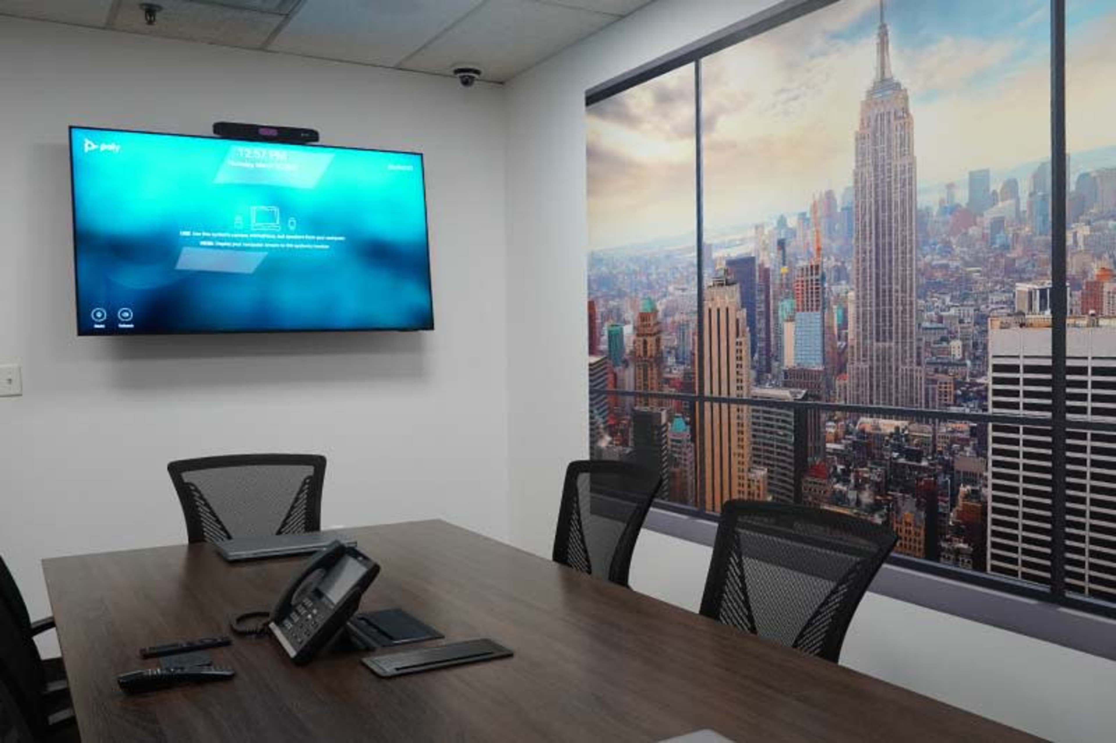 A modern conference room features a large screen displaying a virtual meeting interface, alongside a panoramic wall mural of the New York City skyline with the Empire State Building.