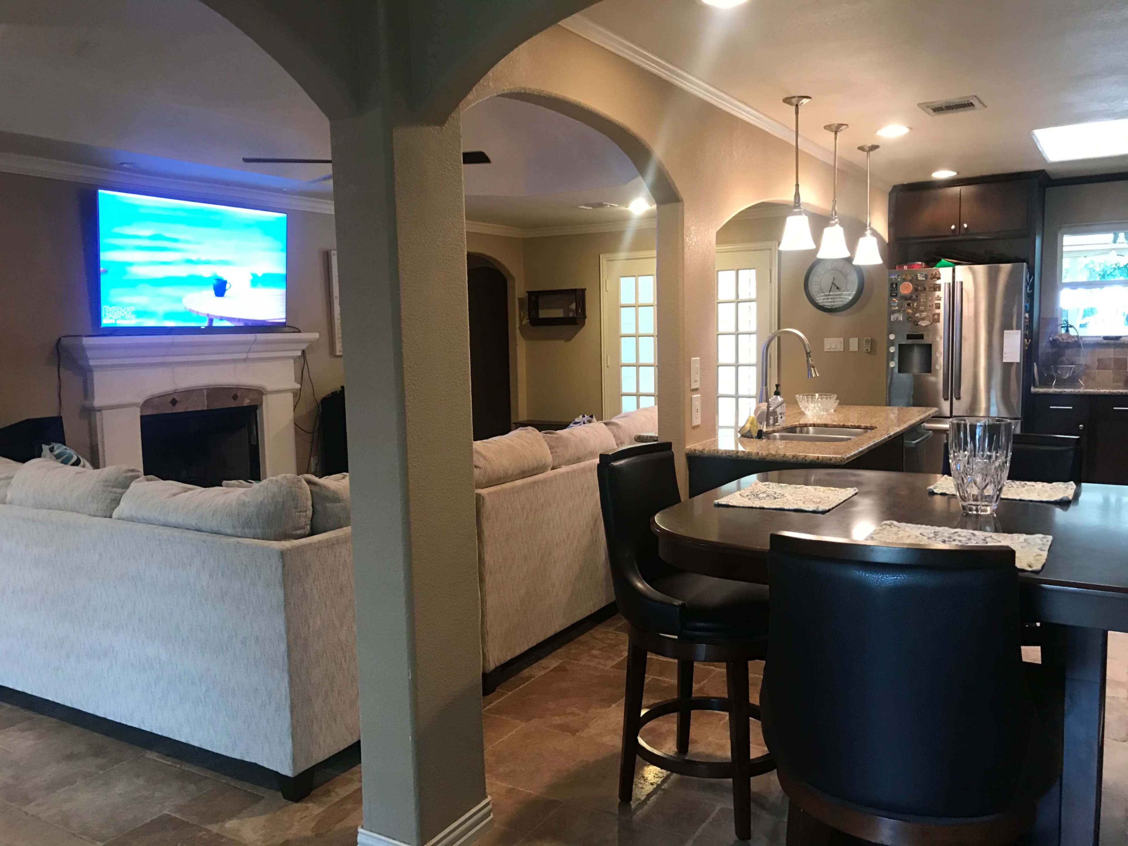 A spacious kitchen and living area with a sofa, a dining table, and a television mounted on the wall.