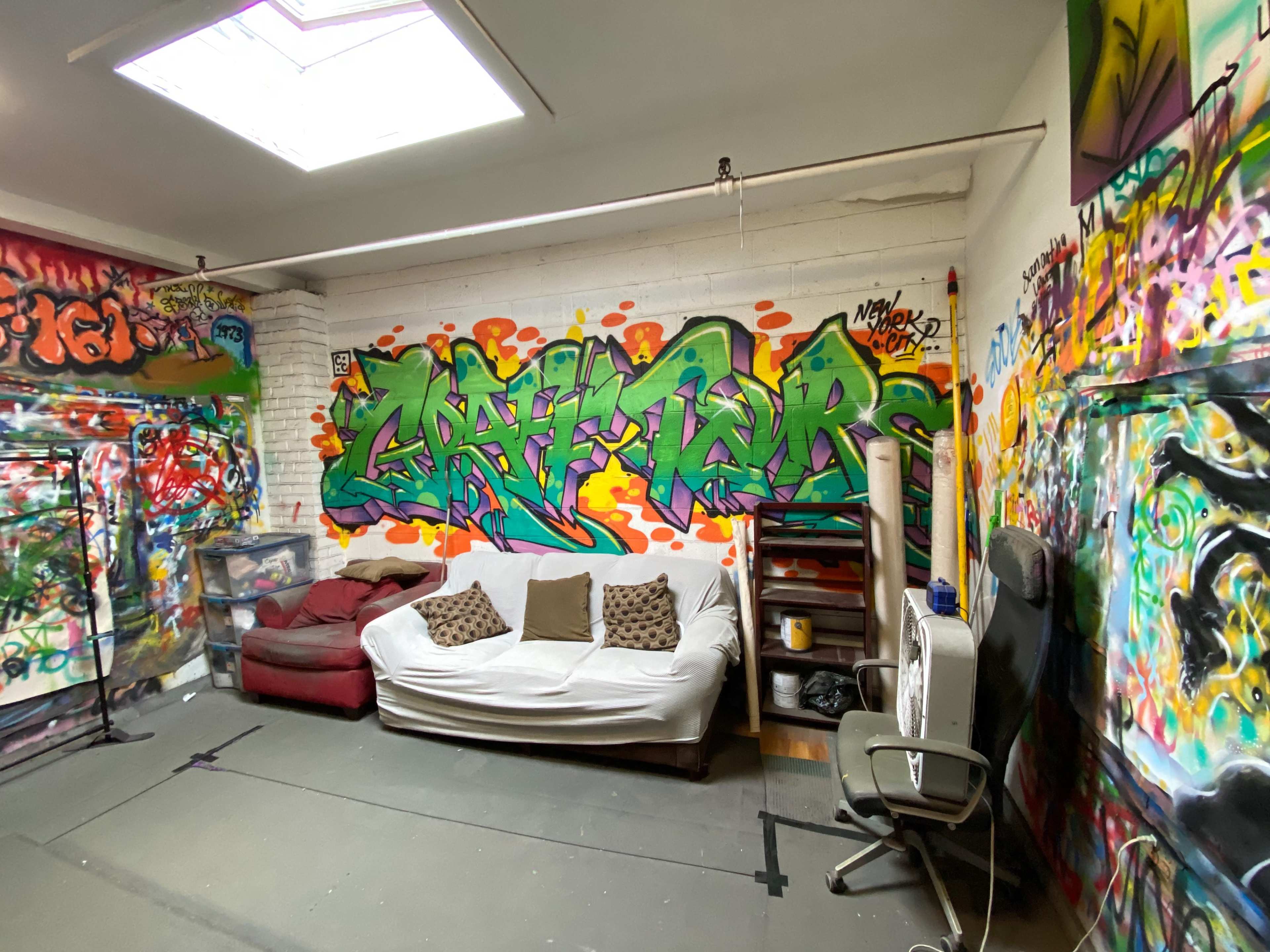 The interior of a room features a white couch, a black chair, and vibrant graffiti on the walls.