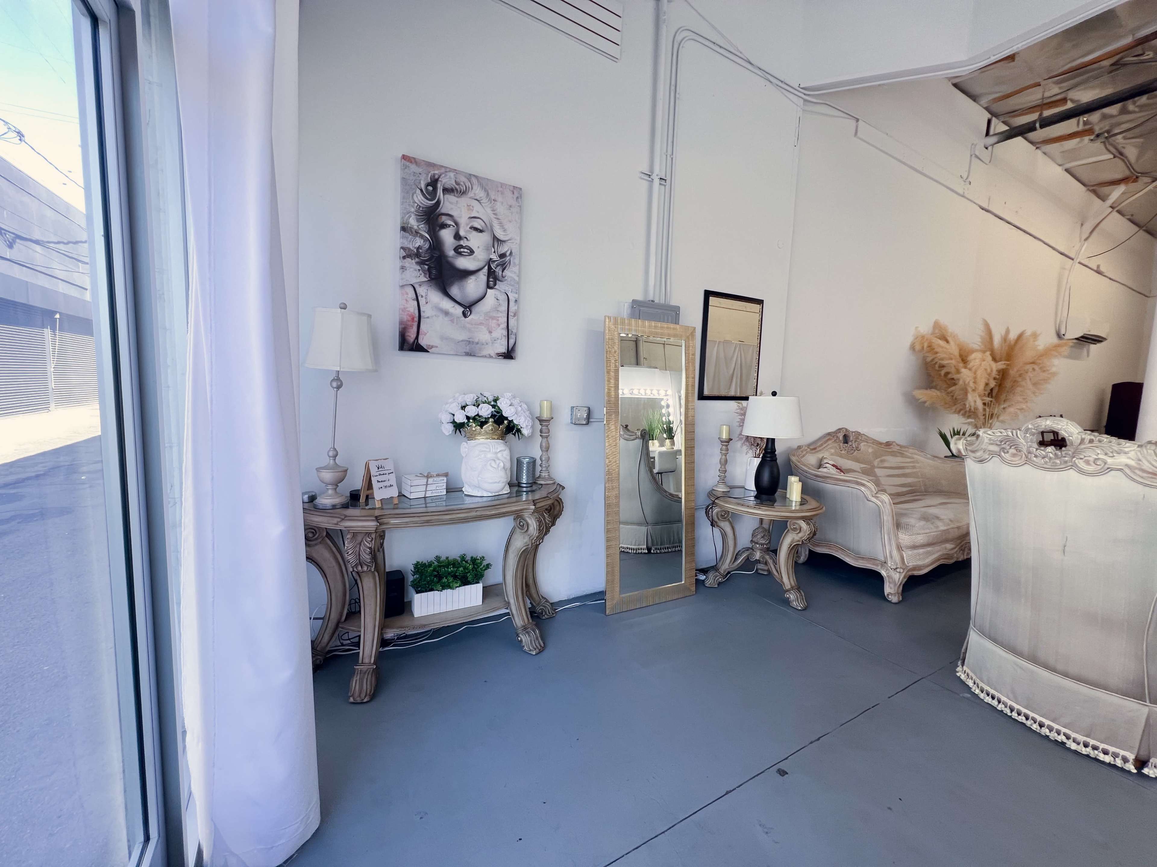 The image shows a stylish interior featuring a large mirror, decorative lamps, a bed, and a framed artwork of a woman on the wall.