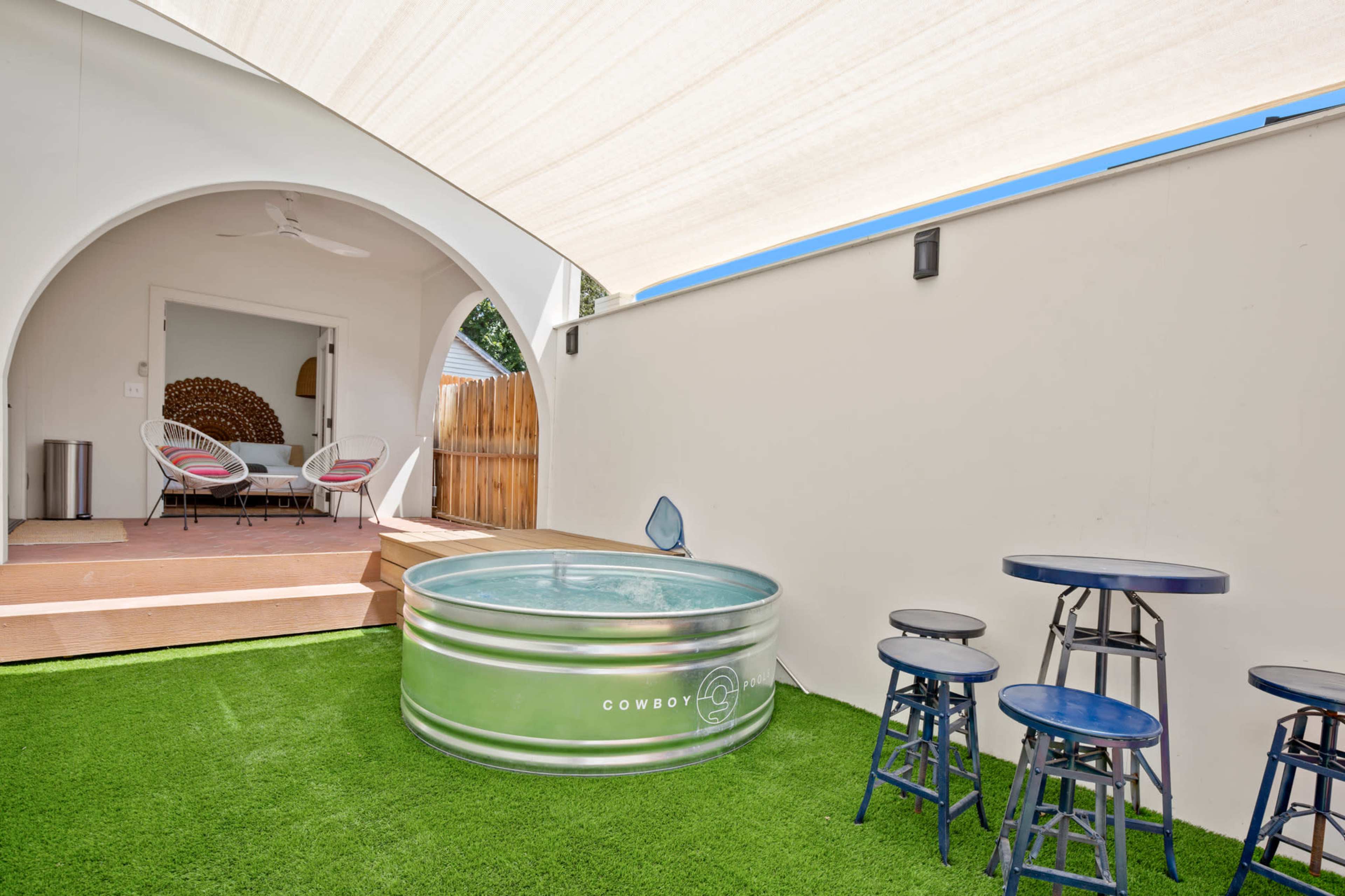 The image shows a backyard area featuring a metal water tank, artificial grass, and outdoor seating under a shaded patio.