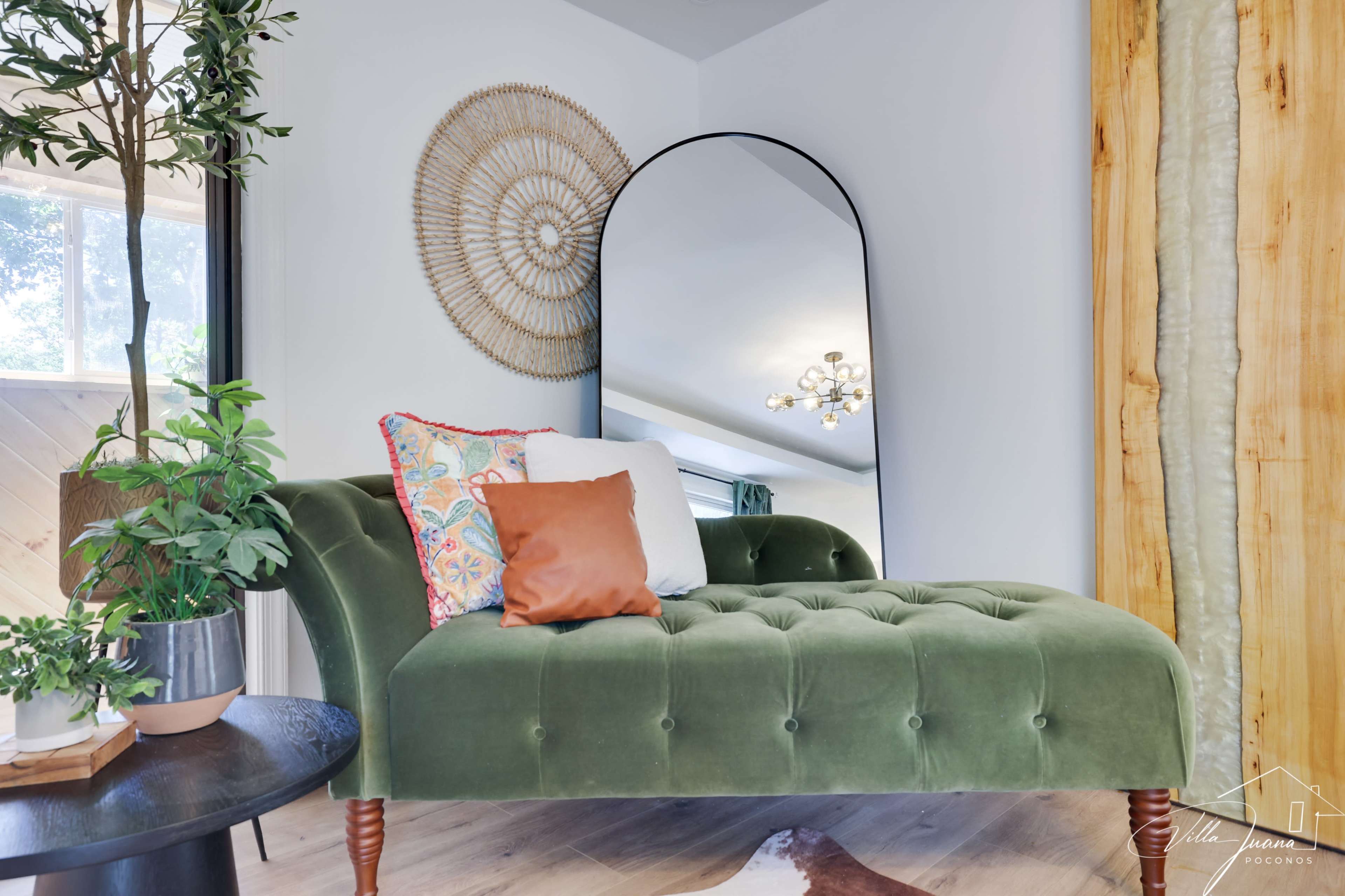 The image shows a green chaise lounge with decorative pillows, a round mirror above it, and a wooden wall on one side.