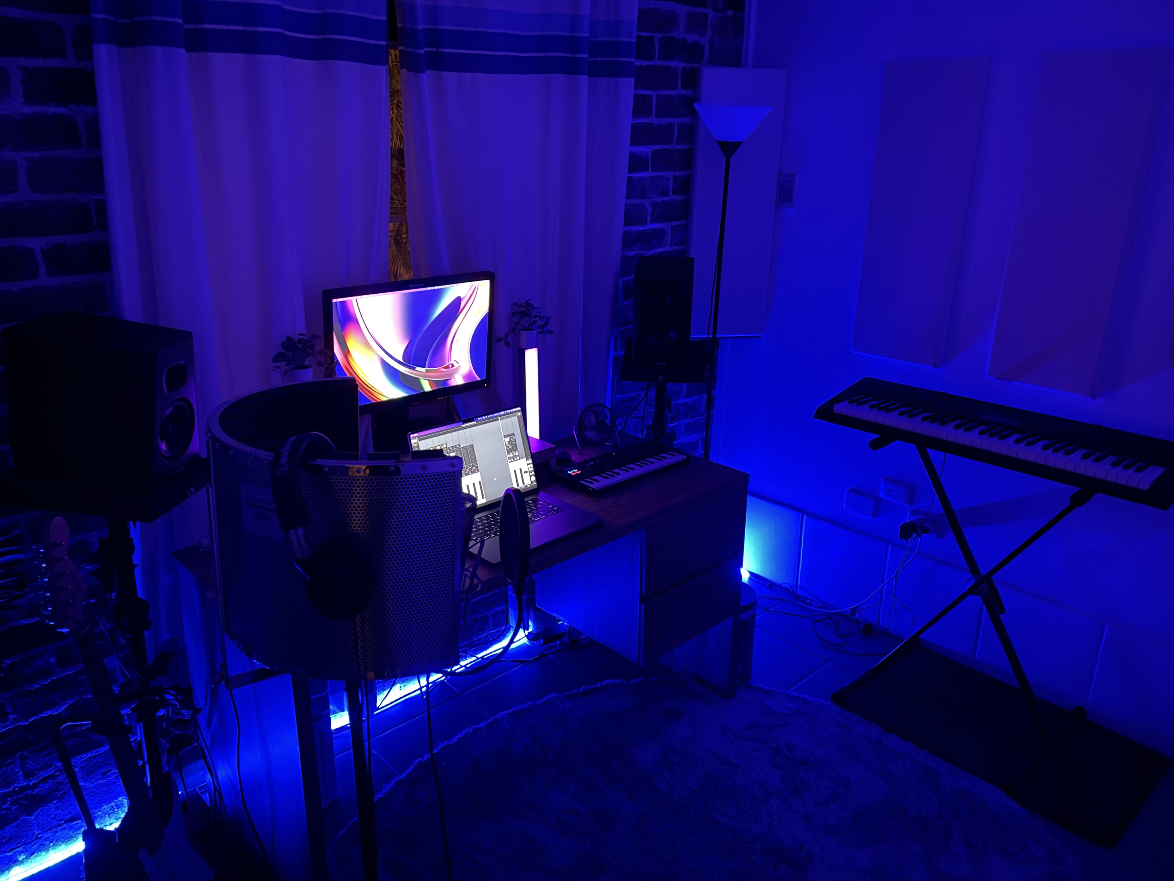 A music production studio with a desk, computer monitor, keyboard, speakers, and ambient lighting in blue tones.