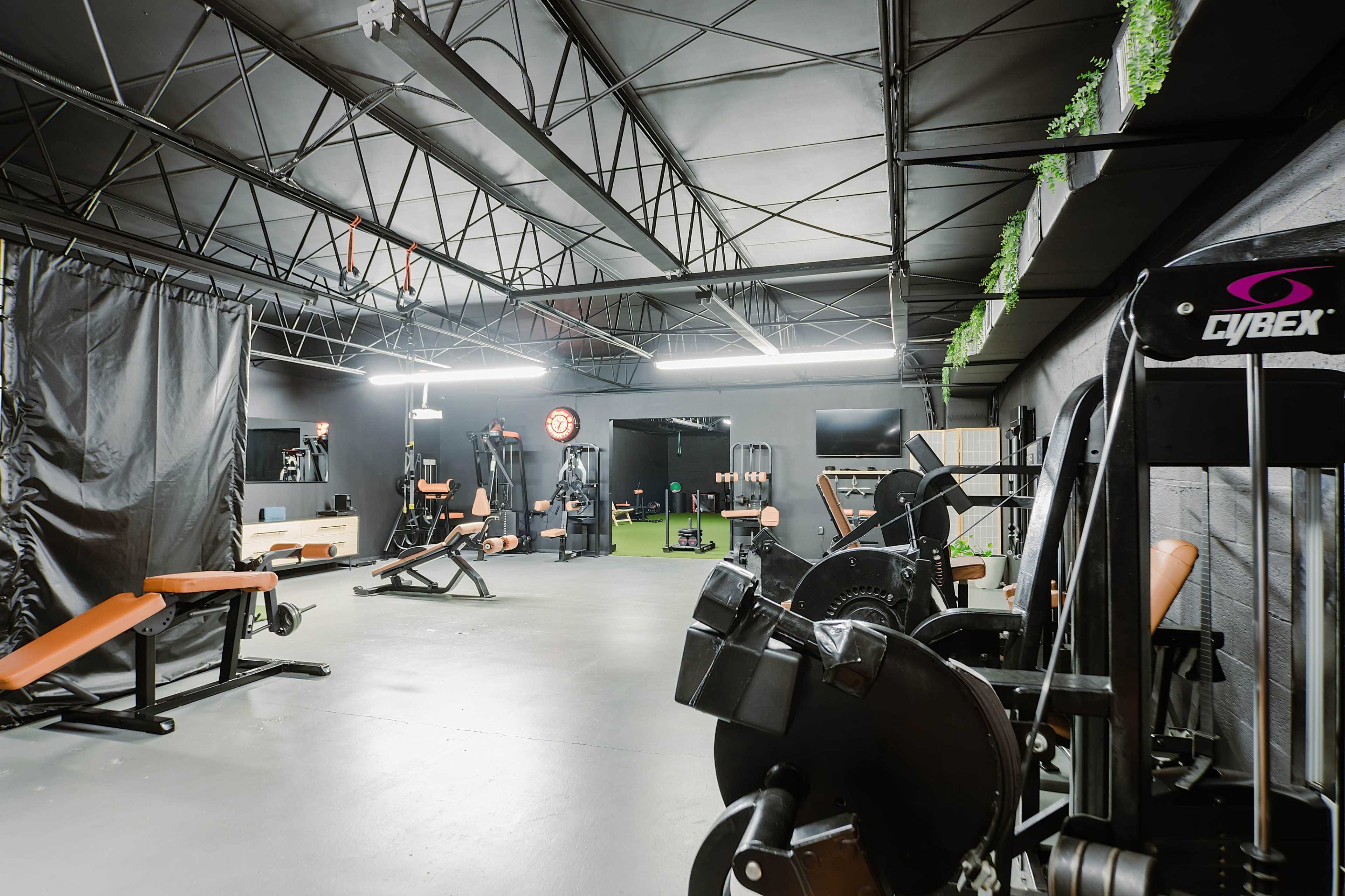 The image shows a spacious gym with various workout equipment and a black ceiling.