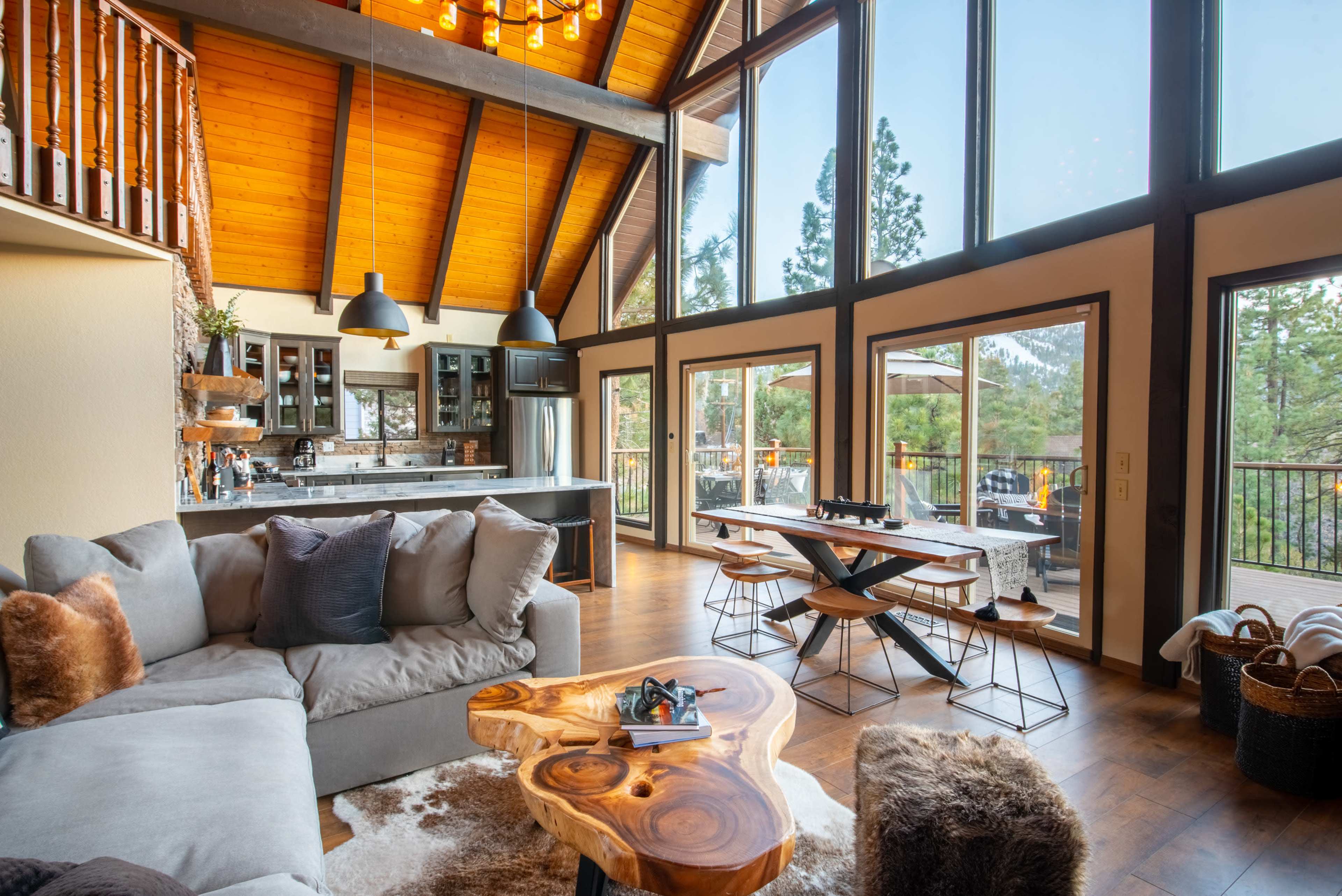 A cozy living space with large windows, a modern kitchen area, a wooden dining table, and a sectional sofa.