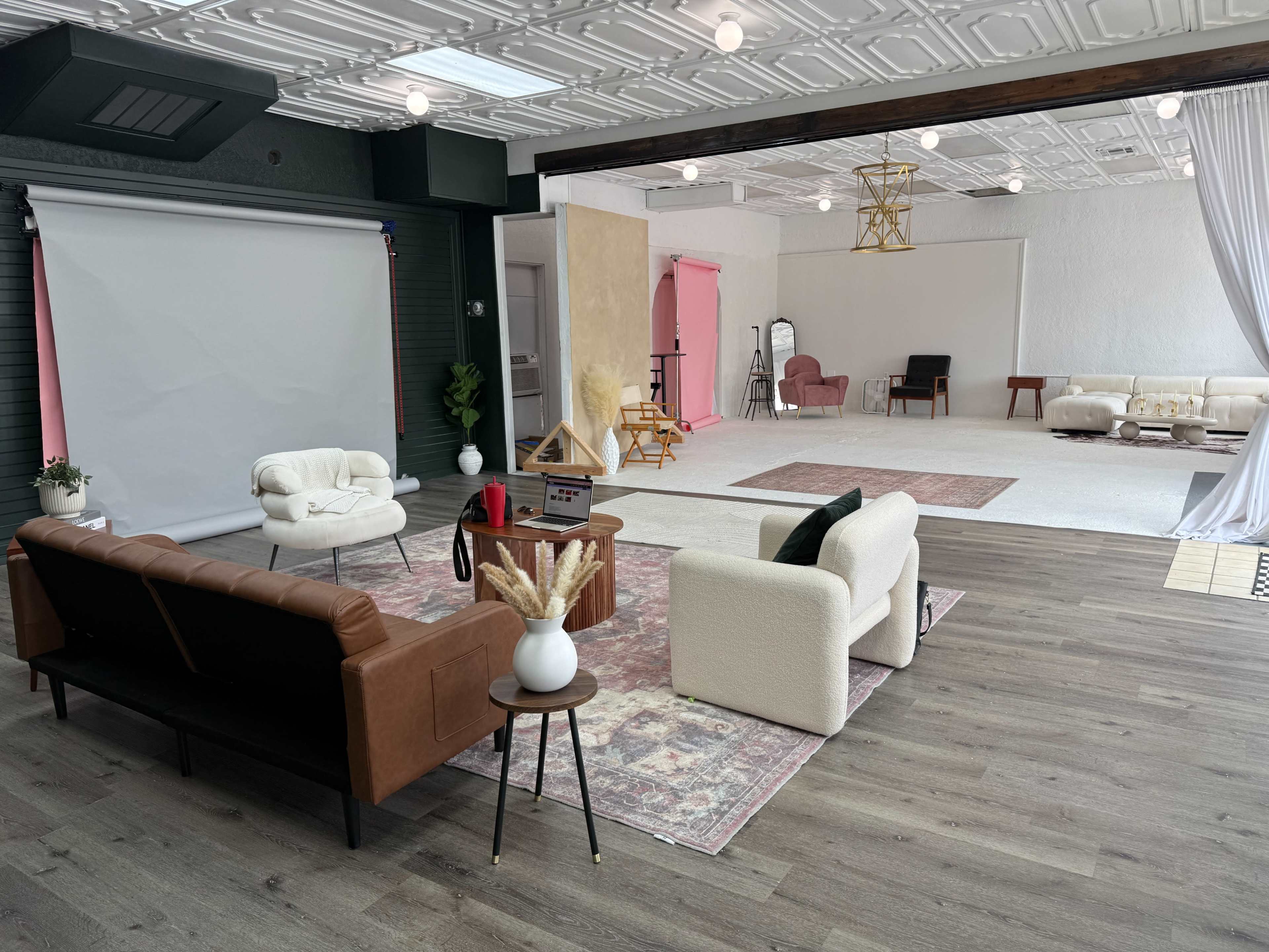 The image shows a spacious photography studio featuring distinct seating areas, a backdrop setup, and various props arranged throughout the room.