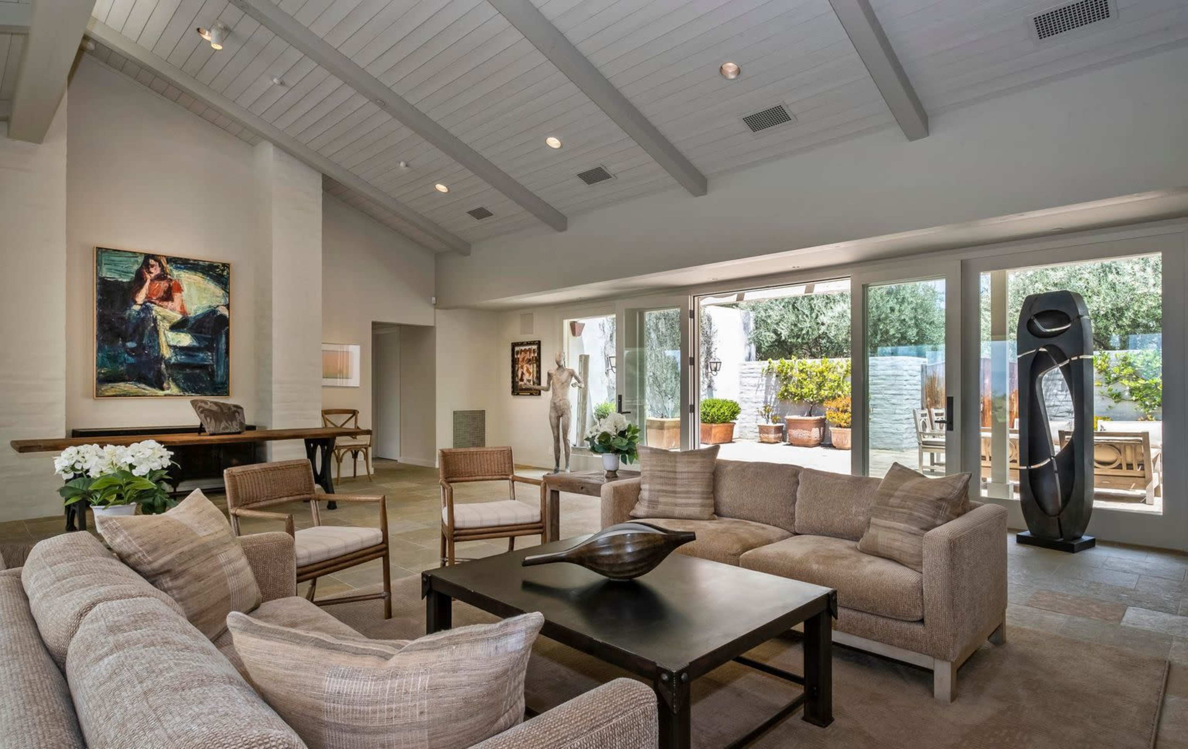 The room features a spacious living area with a light-colored sofa, a dark coffee table, and large windows overlooking a garden.