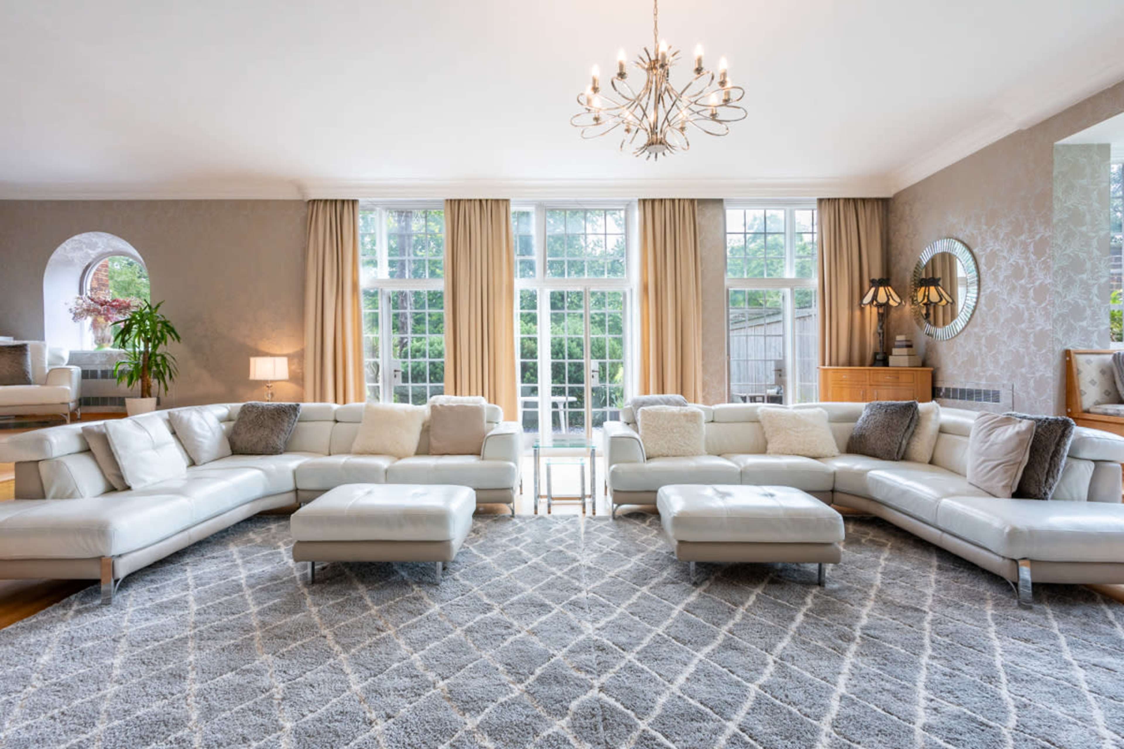 A spacious living room furnished with a large white sectional sofa, a central rug with a geometric pattern, and large windows allowing natural light to fill the space.