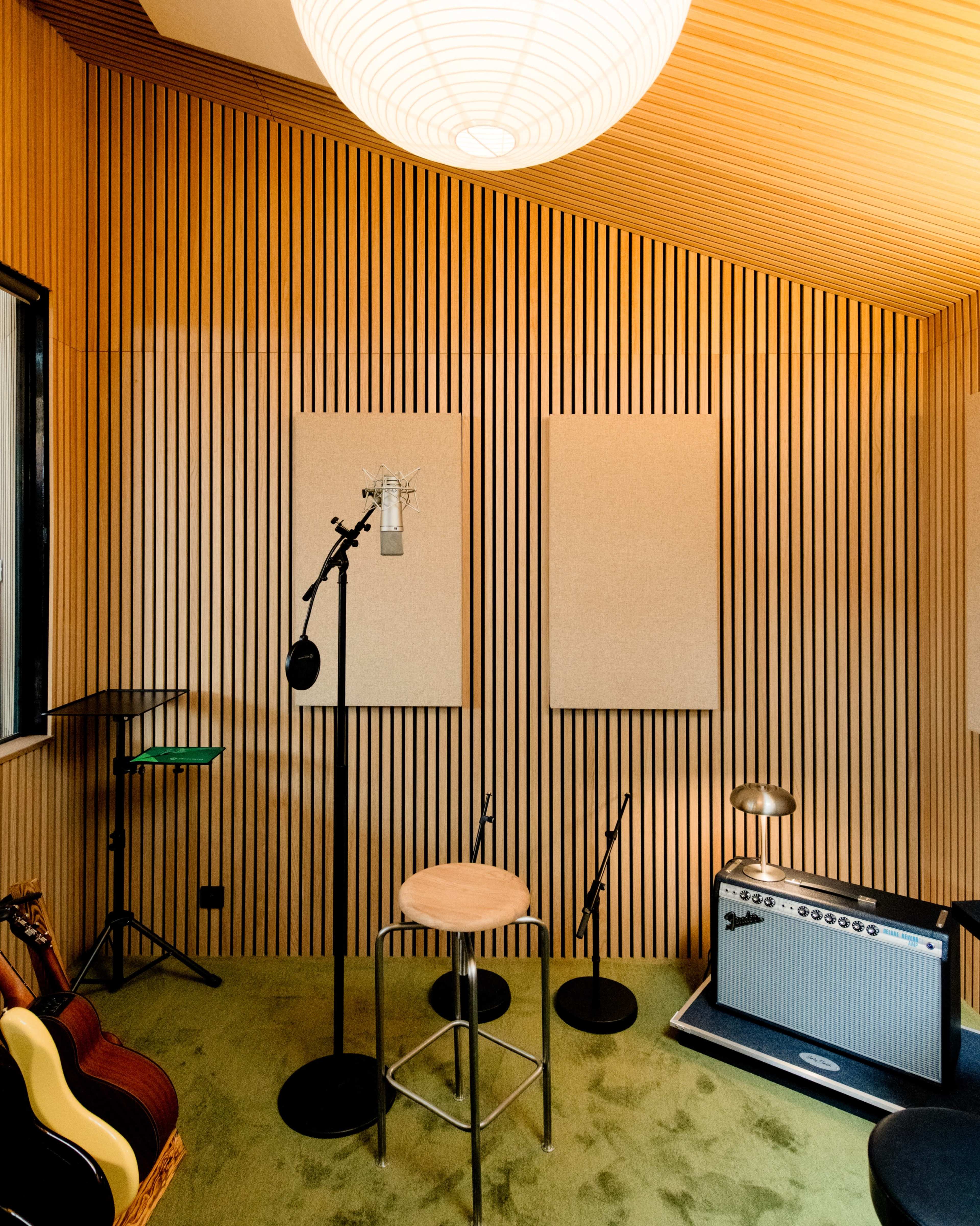 The image shows a well-designed recording studio with wooden slat walls, a microphone setup, and various musical instruments, including a guitar and amplifier.