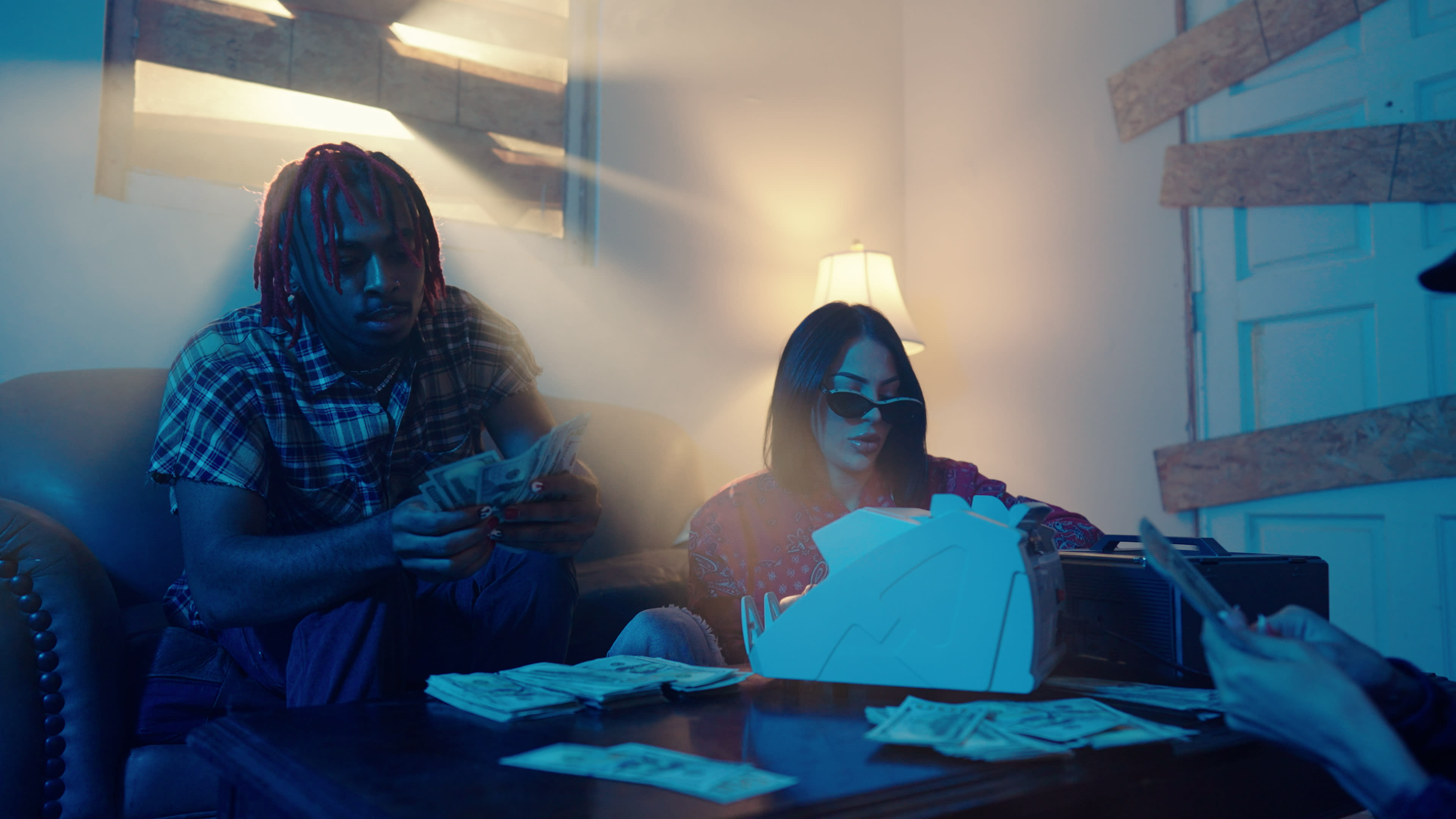 A man and a woman sort and count stacks of cash in a dimly lit room.