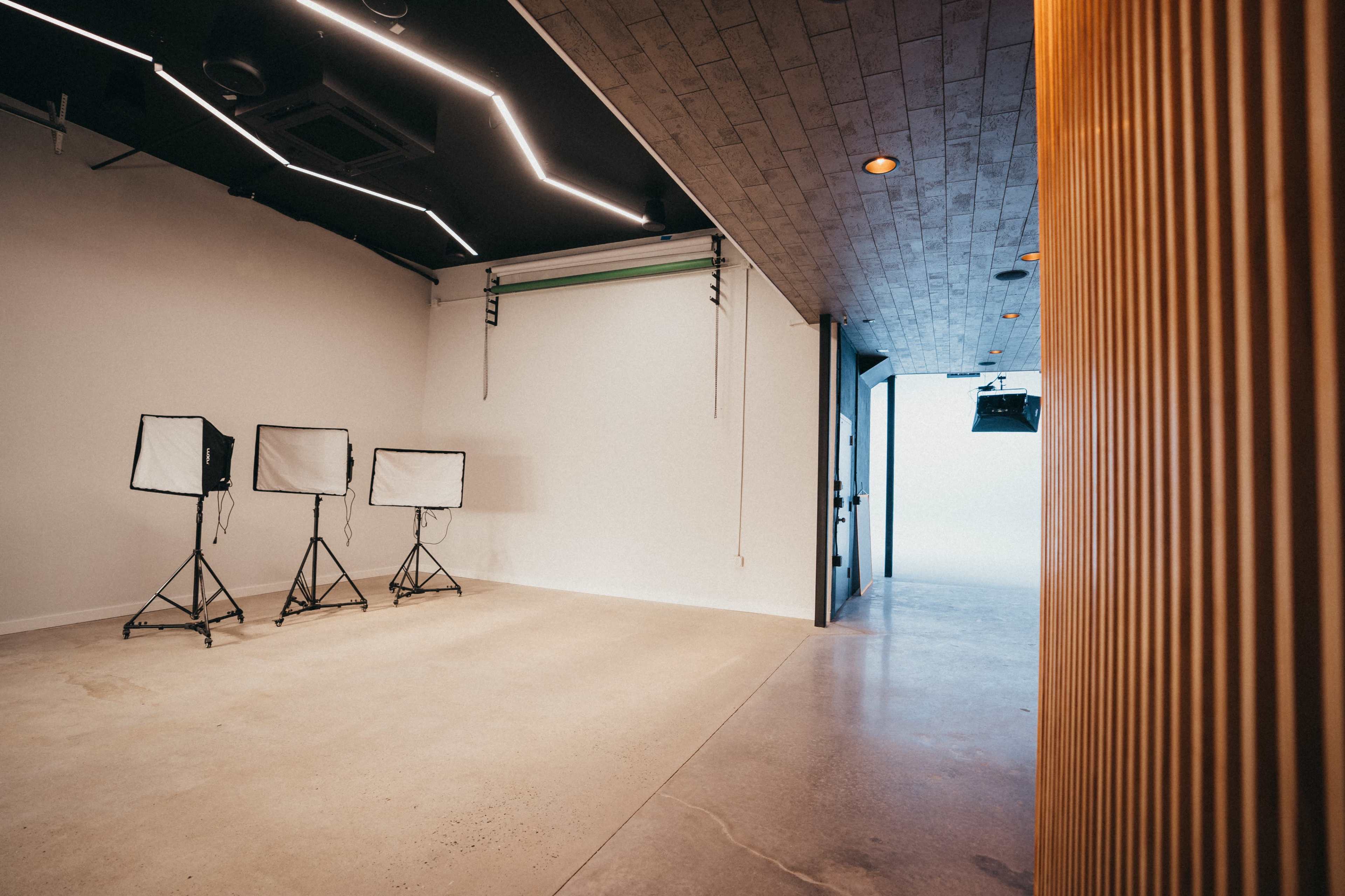 A photography studio with three lighting setups on stands and a seamless backdrop at the far end.