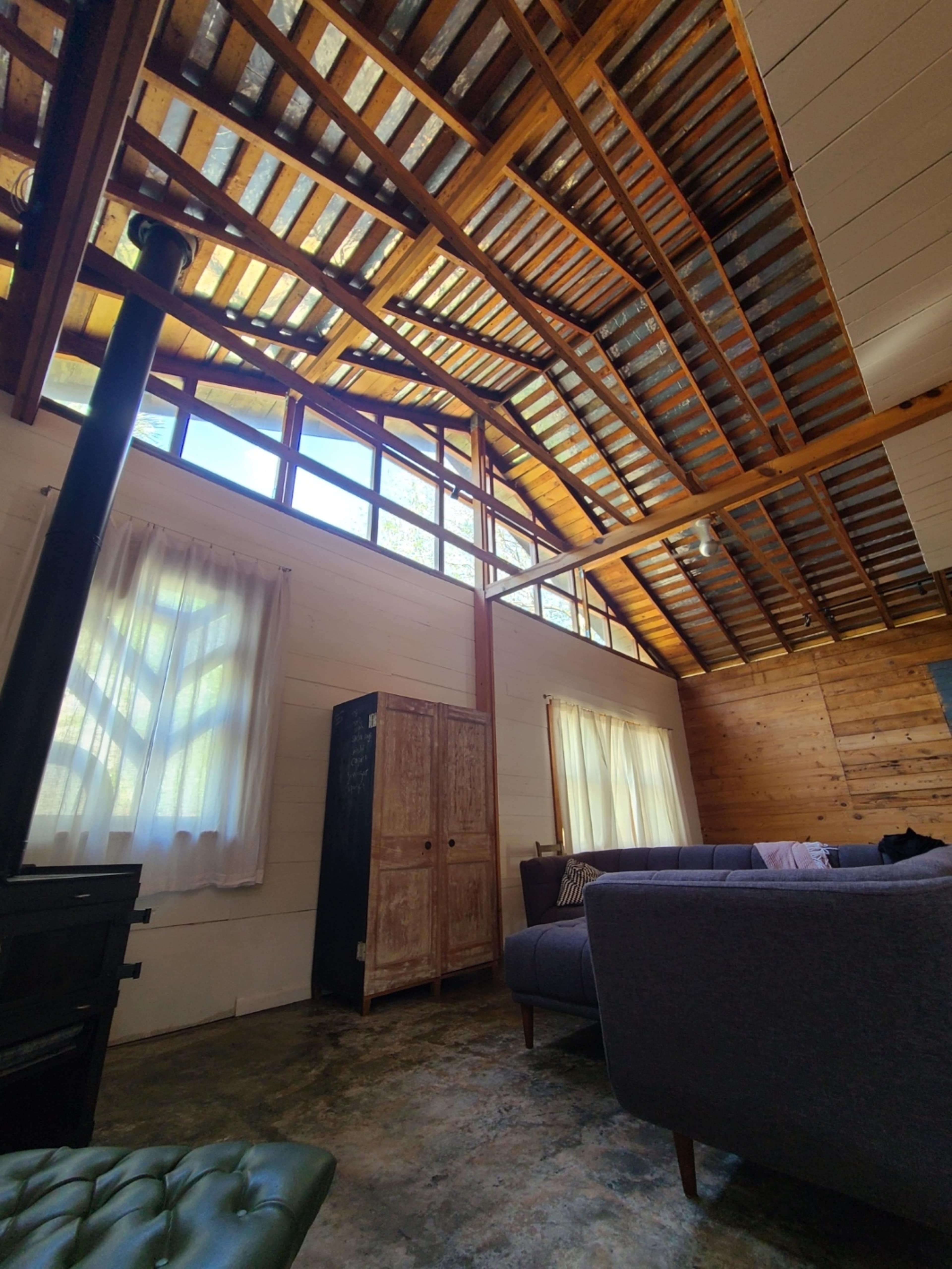 A cozy living room with high wooden ceilings, large windows, and a mixture of rustic and modern furniture.