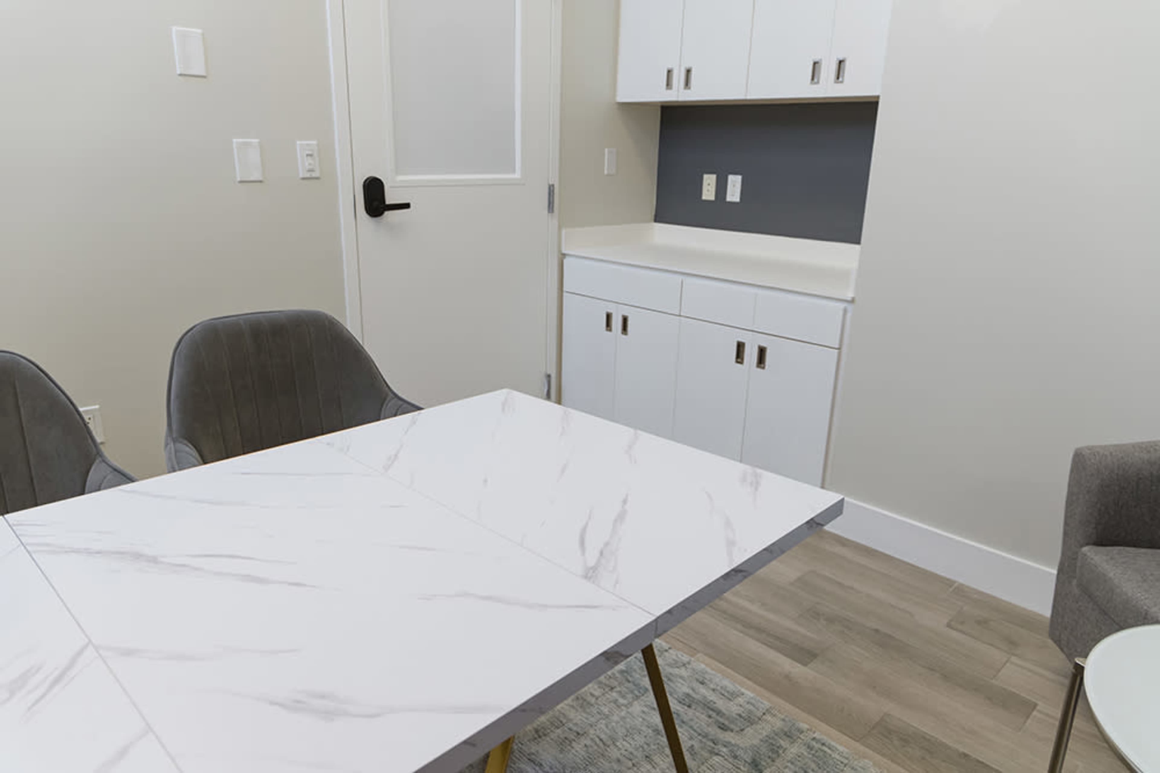 A small dining area featuring a marble-top table with two gray chairs and a cabinet against the wall.