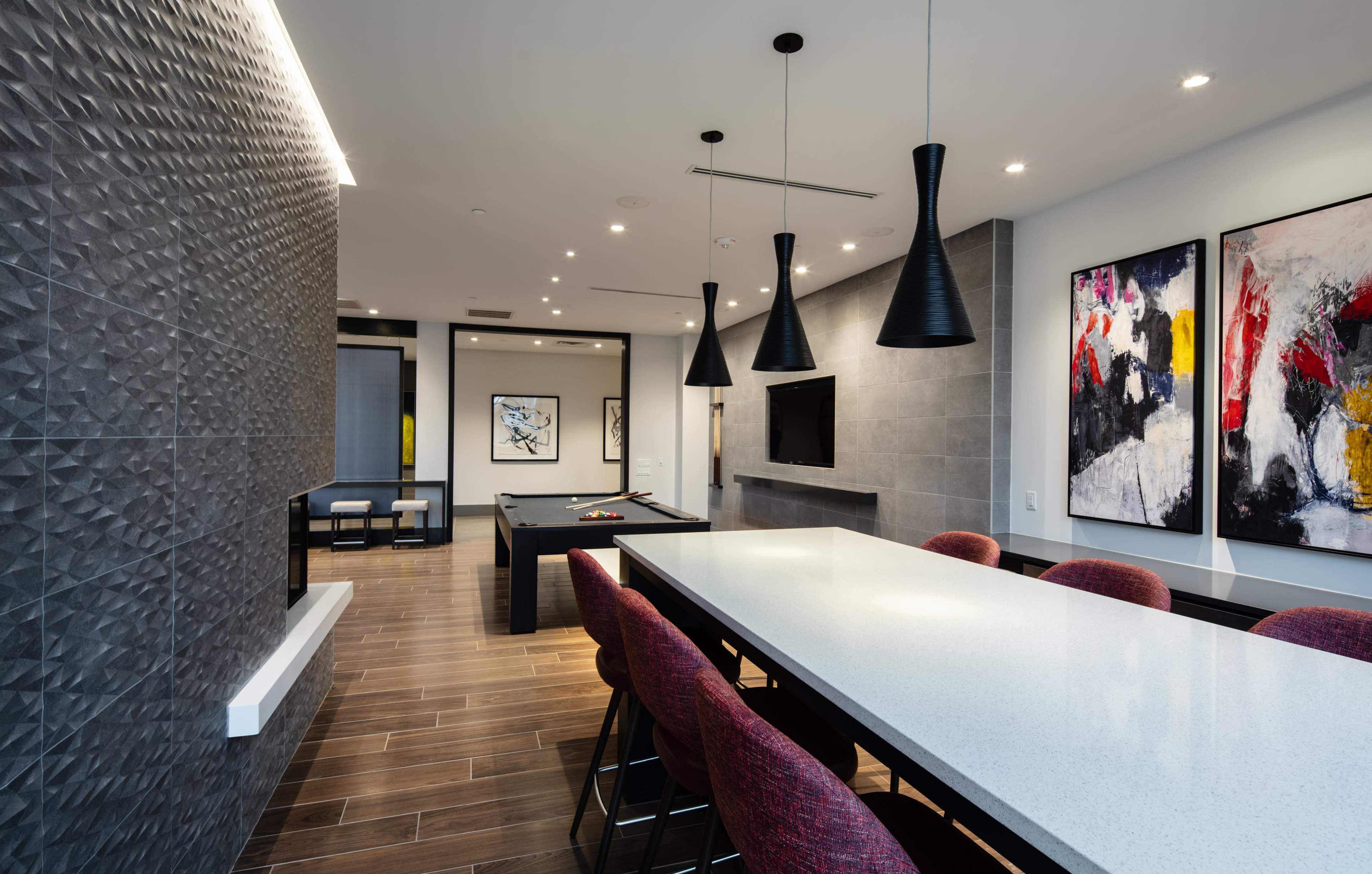A contemporary dining area with a long table and pendant lights, leading into a game room featuring a pool table and abstract artwork on the walls.