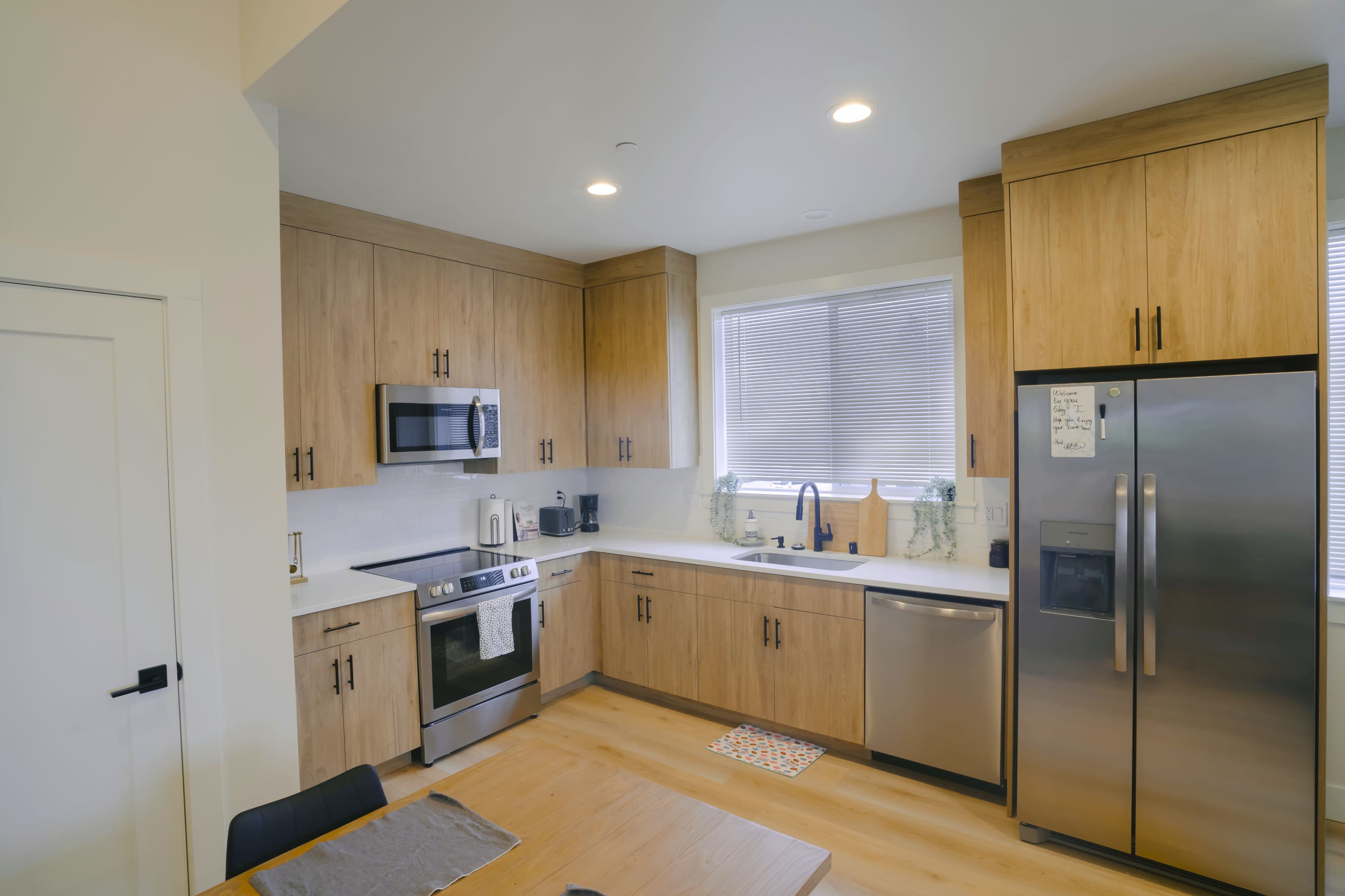 The image shows a modern kitchen with wooden cabinets, stainless steel appliances, and a window above the sink.