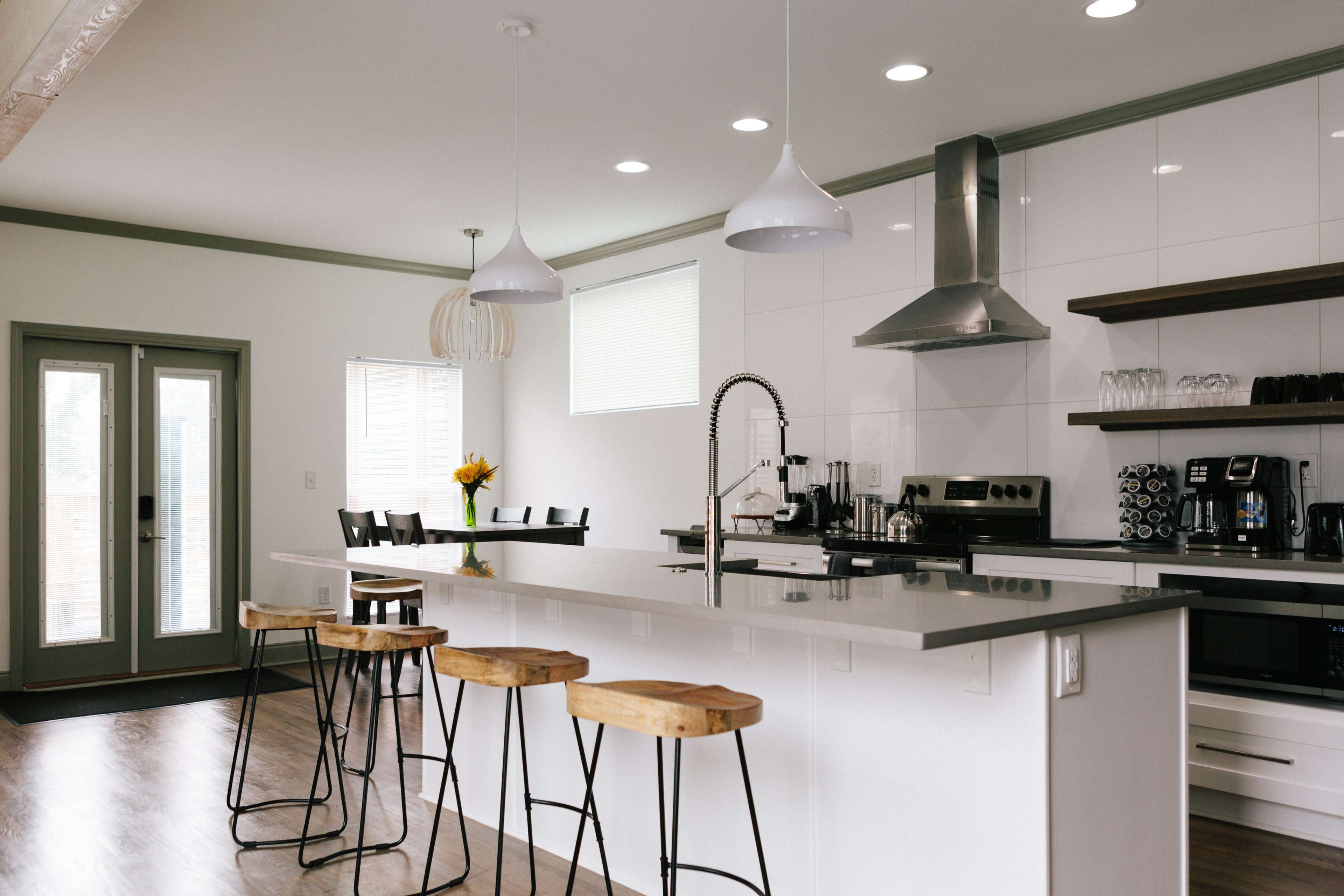 A modern kitchen features sleek white cabinetry, stainless steel appliances, and a large island with wooden stools.