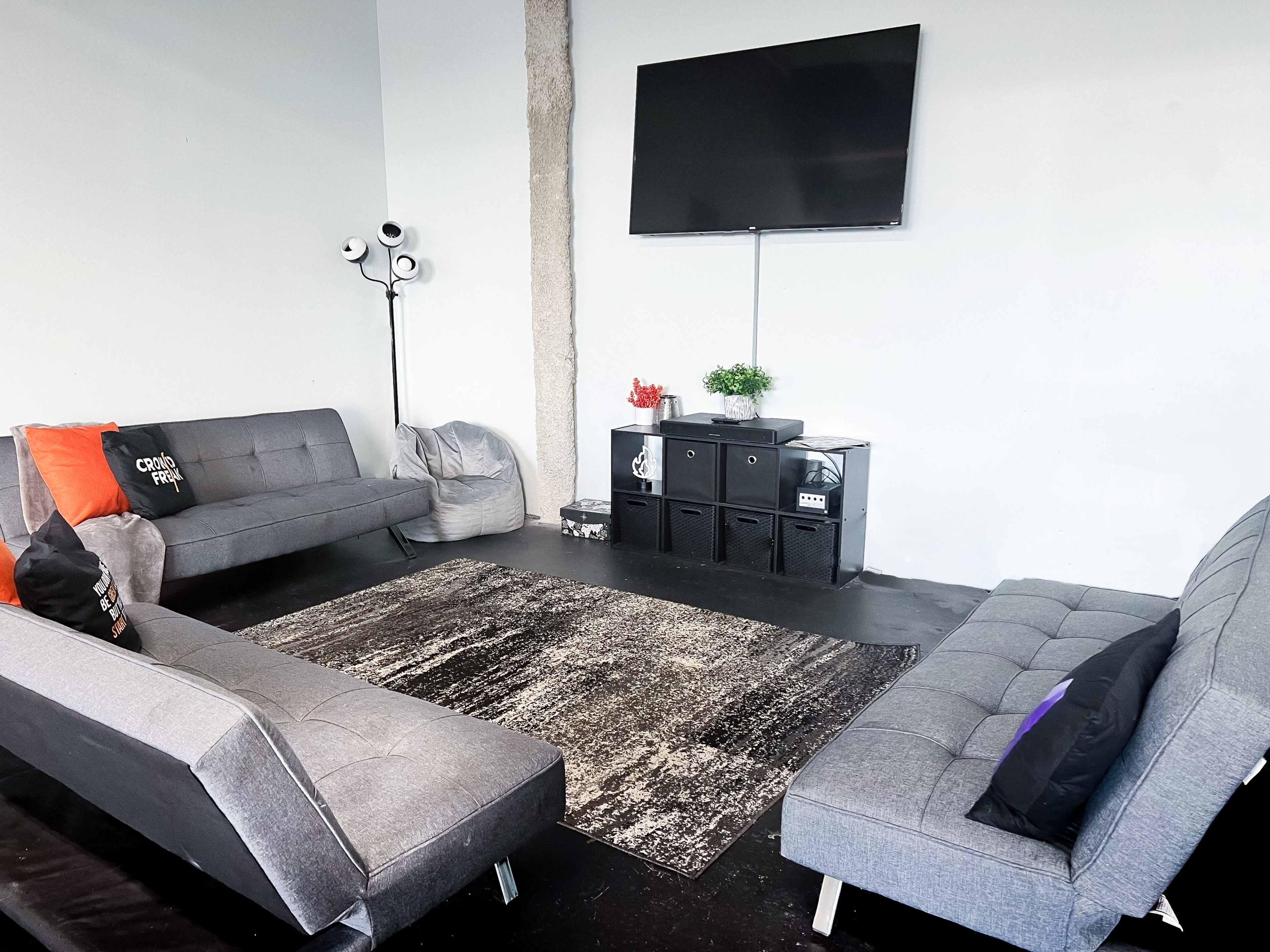 A modern living space with two gray sofas, a large area rug, a wall-mounted television, and a set of black storage units.