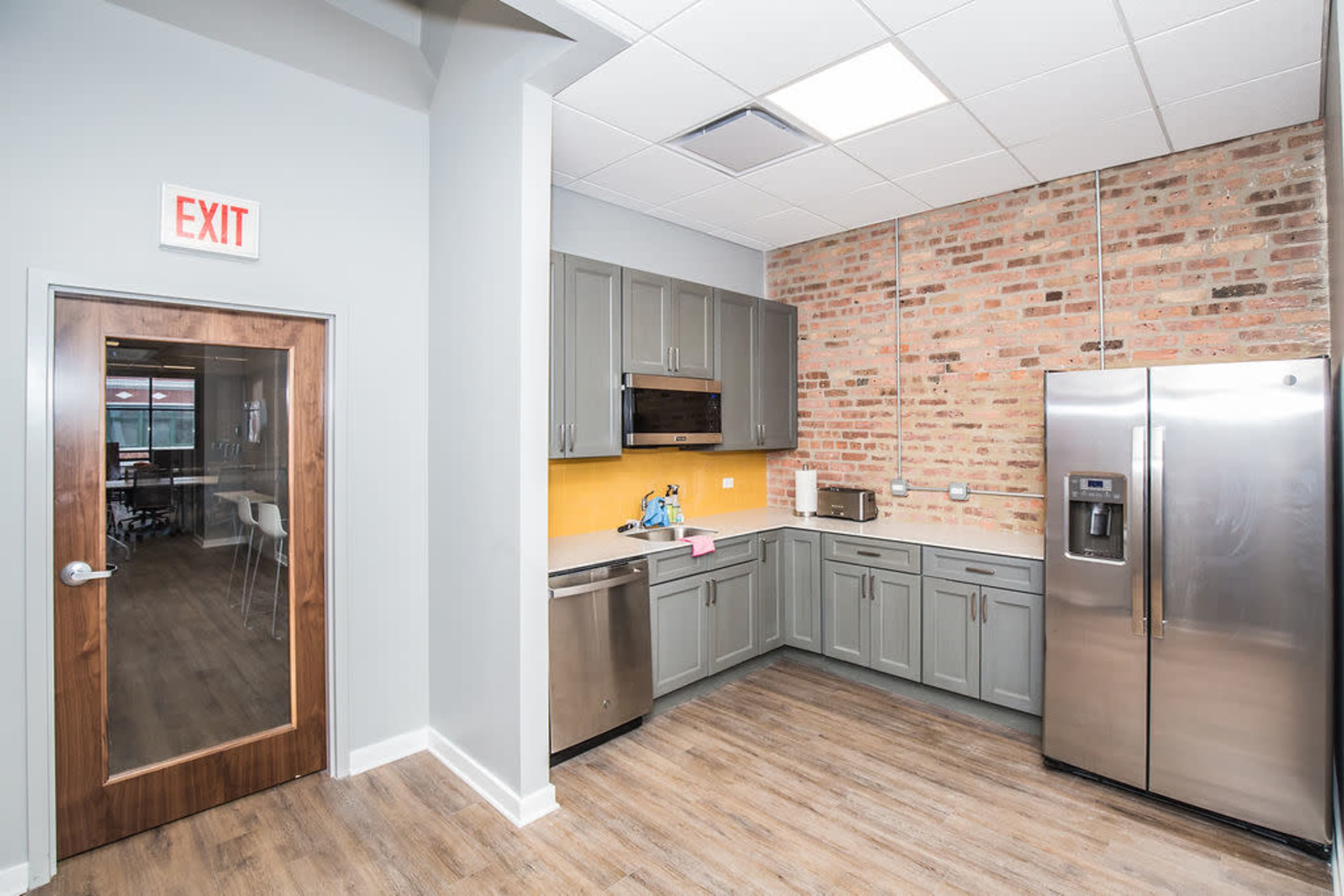 A modern kitchen with gray cabinets, stainless steel appliances, and a brick accent wall.