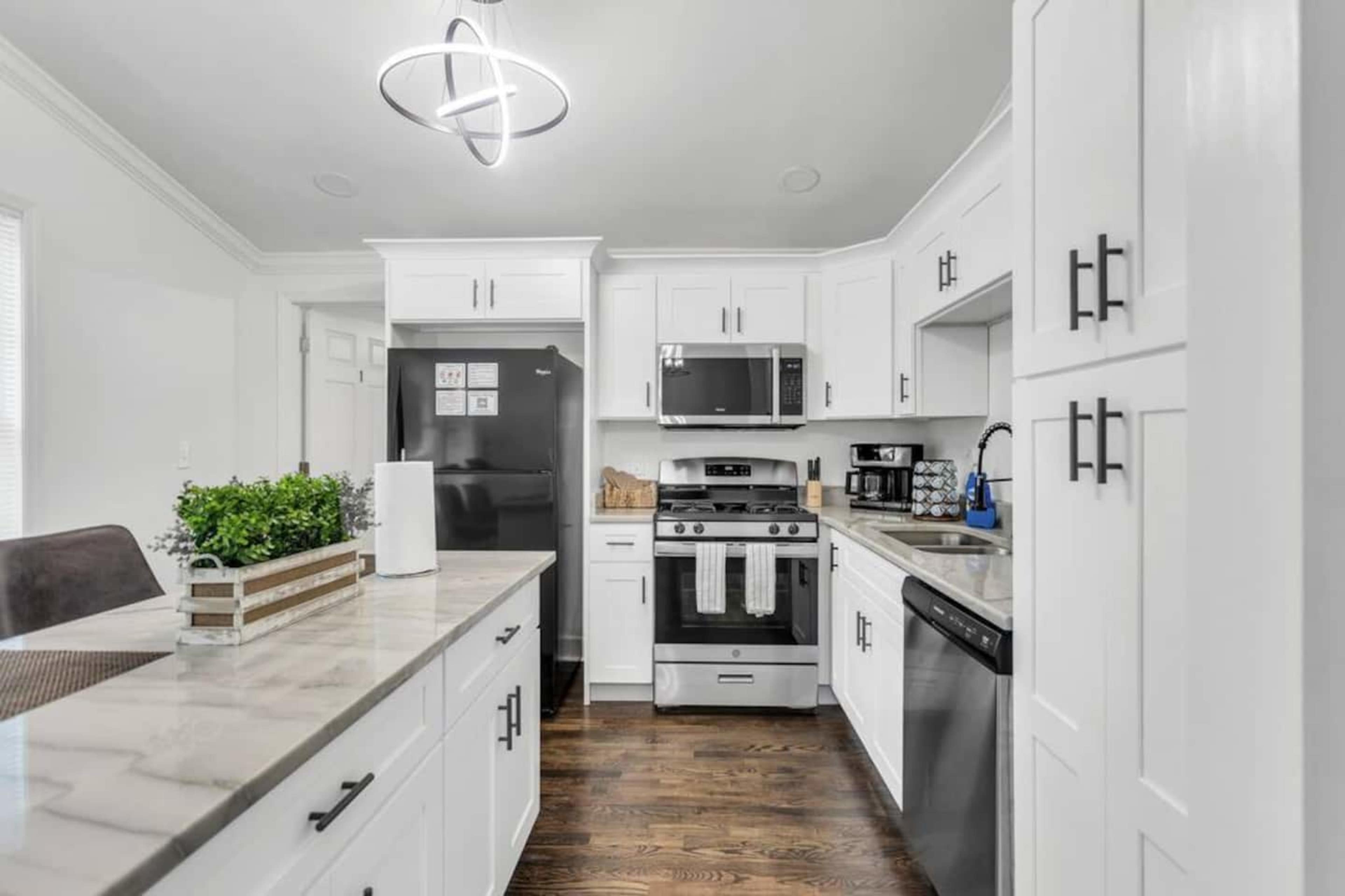 A modern kitchen features white cabinetry, stainless steel appliances, and a marble countertop with a raised planter and a pendant light overhead.
