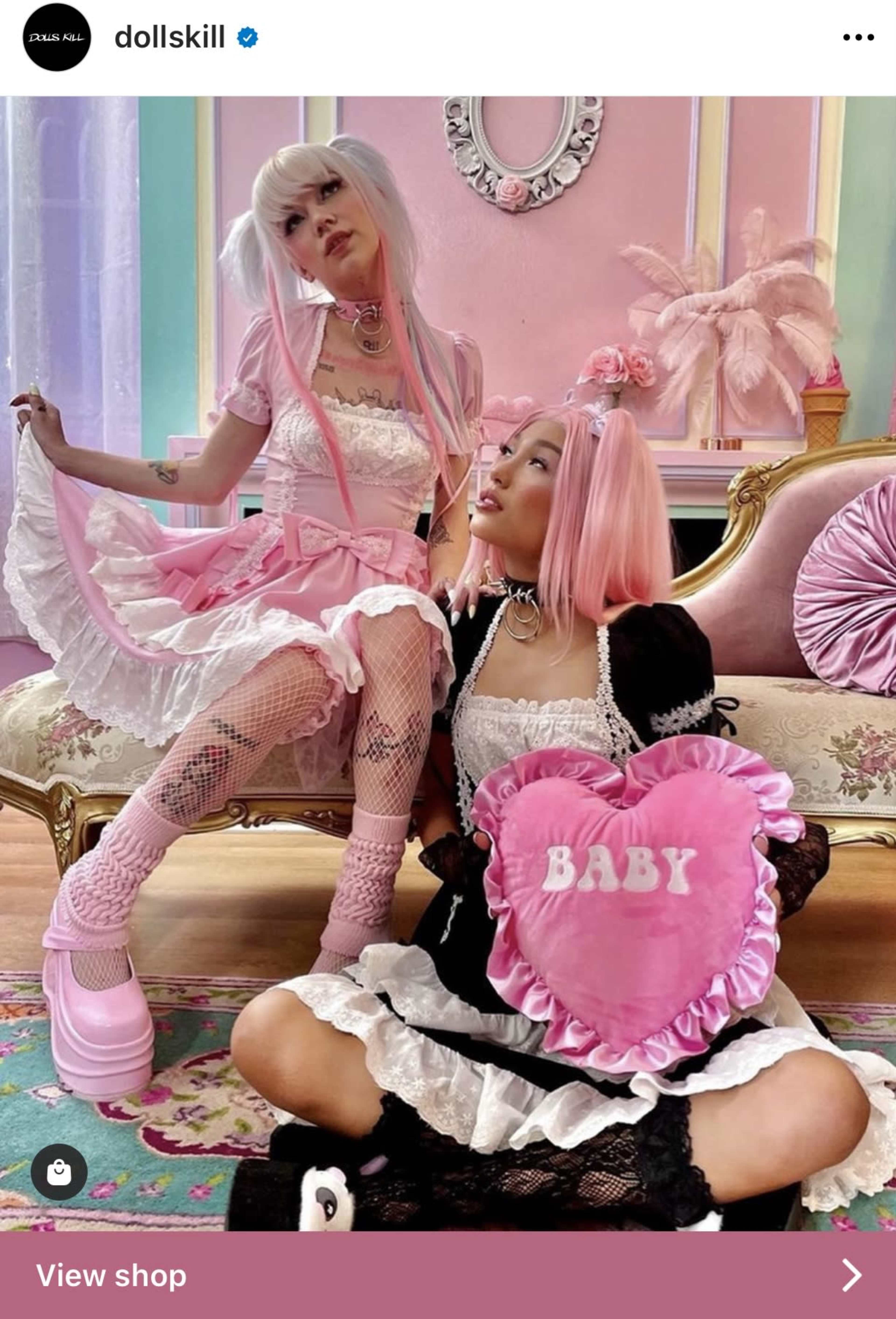 Two young women dressed in pastel-colored outfits and platform shoes pose on a vintage sofa in a brightly decorated room.
